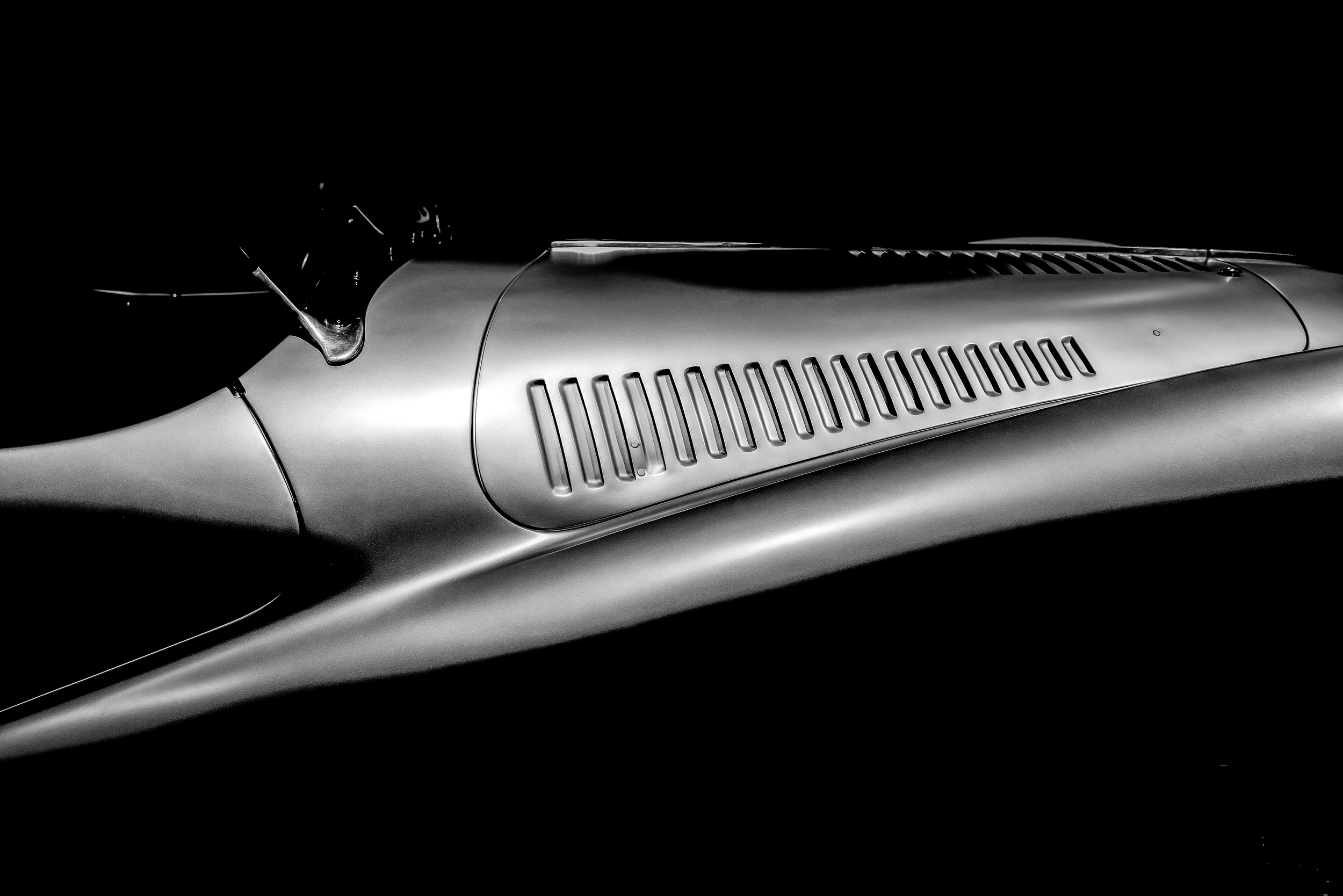 Close-up of a vintage racing car's sleek metallic body with air vents, photographed in black and white.