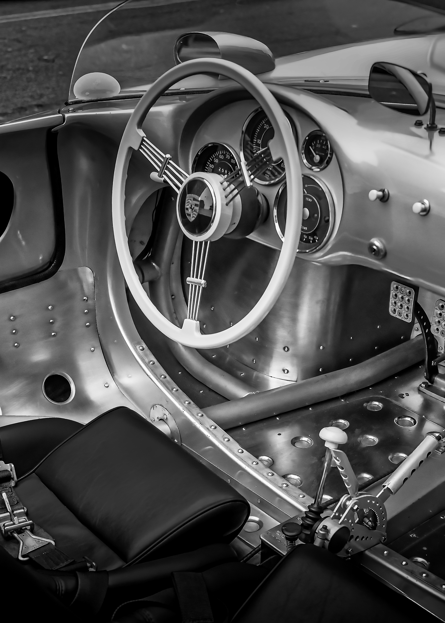 Interior of a vintage Porsche race car featuring a minimalist dashboard, metal body panels, a racing seat, and a manual gear shifter.