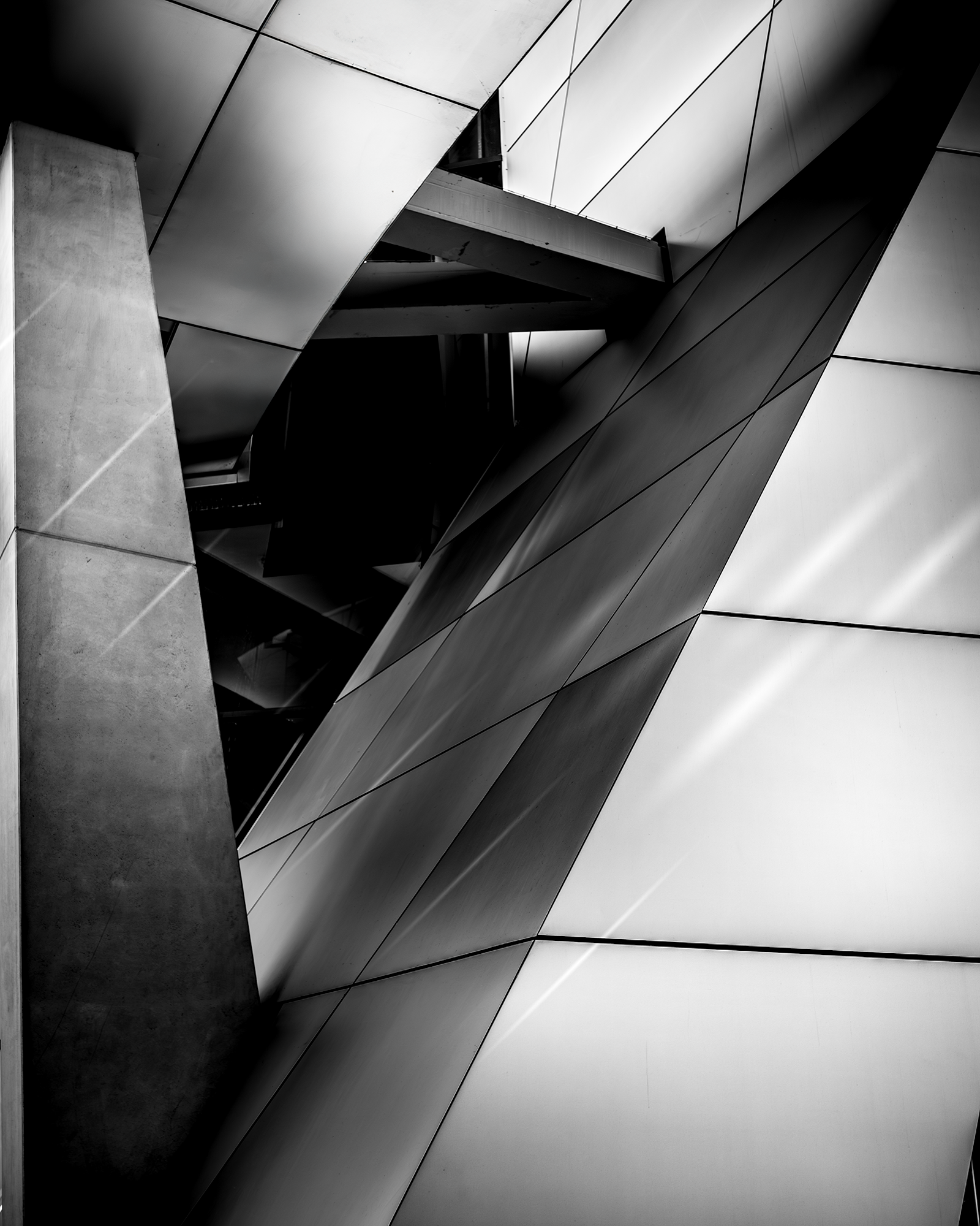 Black and white photo of modern building with angular geometric shapes, metal panels, and contrasting light and shadow.