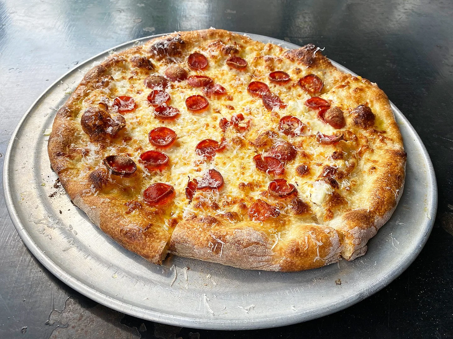 A pepperoni pizza on a metal tray placed on a dark table.