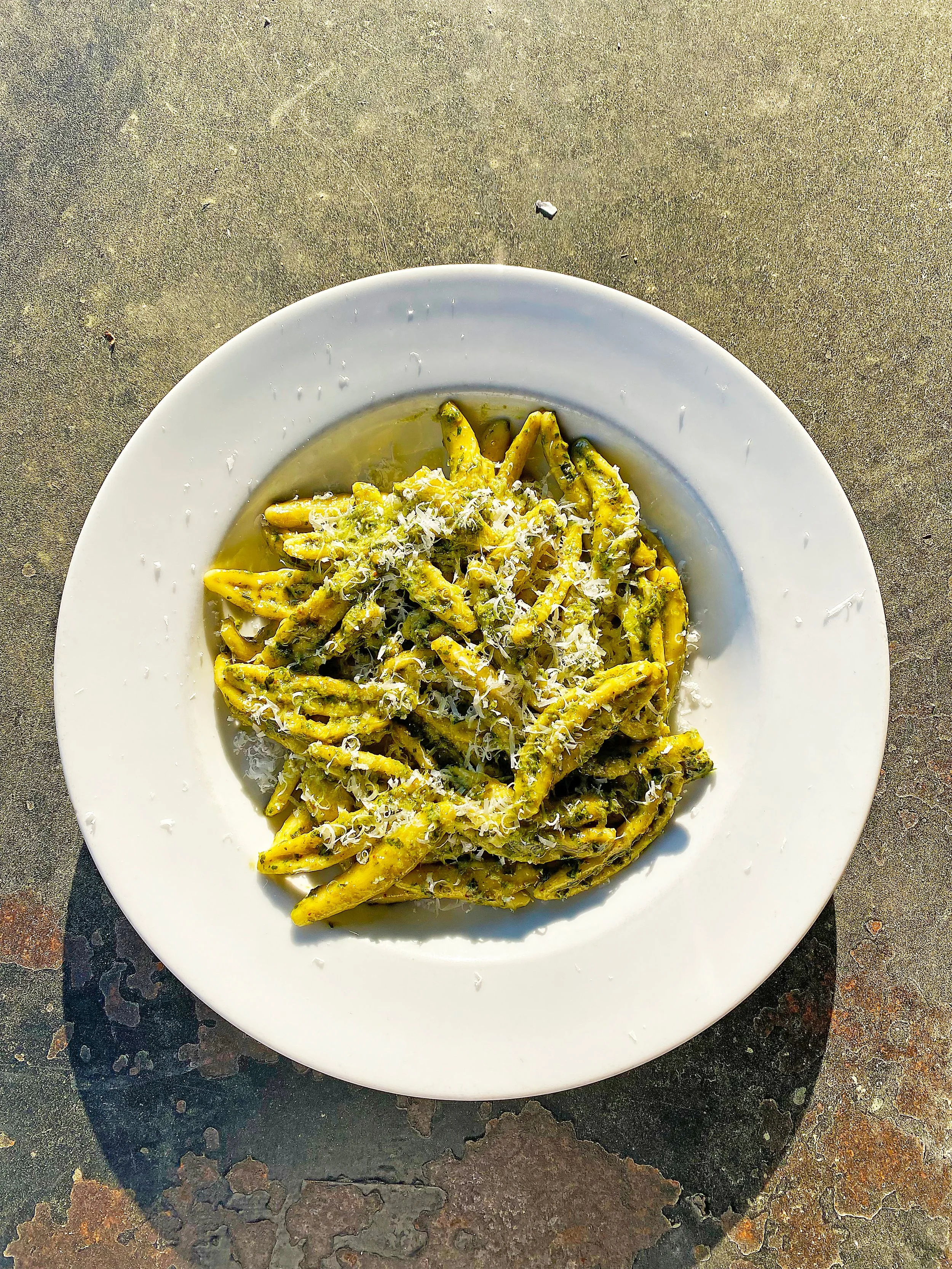 Plate of yellowish-green pasta with shredded cheese on top, placed on a rustic surface.