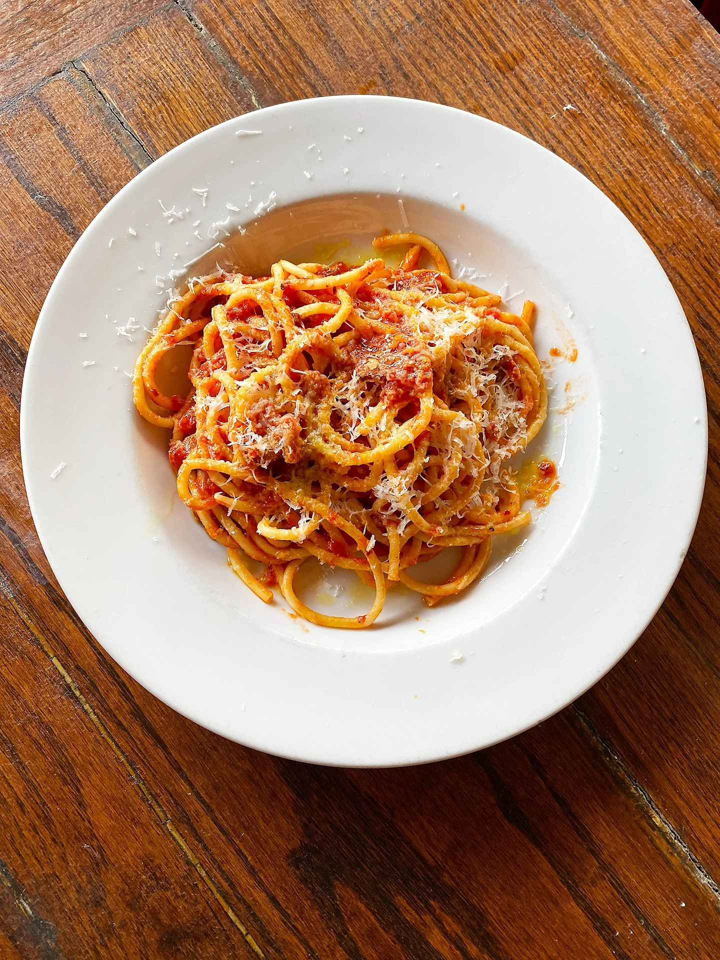 Plate of spaghetti with tomato sauce and grated cheese on a wooden table.