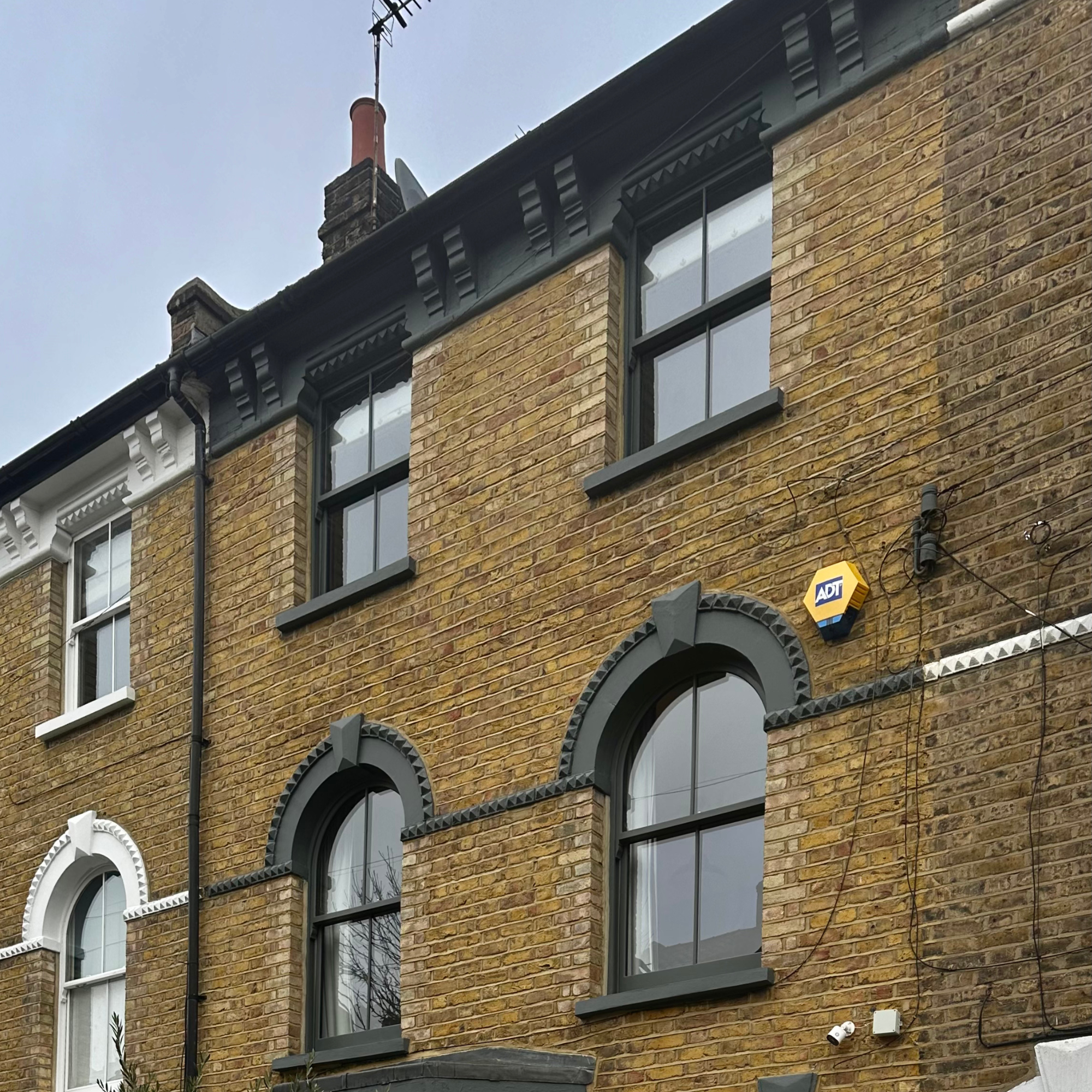 The exterior of a multi-story brick building with black and white window trims and a black decorative cornice. There are multiple handmade bespoke accoya windows