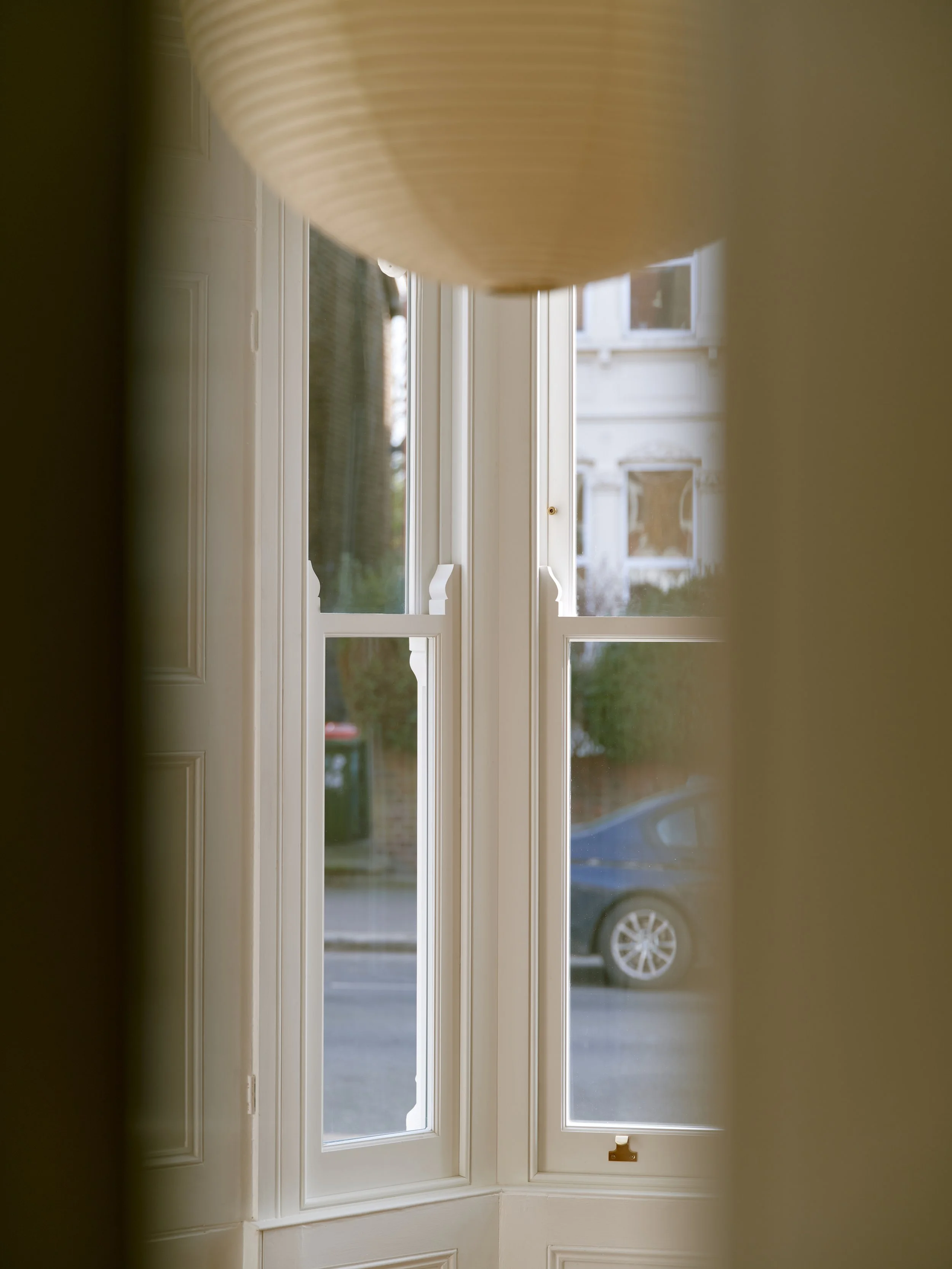 View through a handmade bespoke accoya window with white trim, showing a street with a parked car and a building across the street.