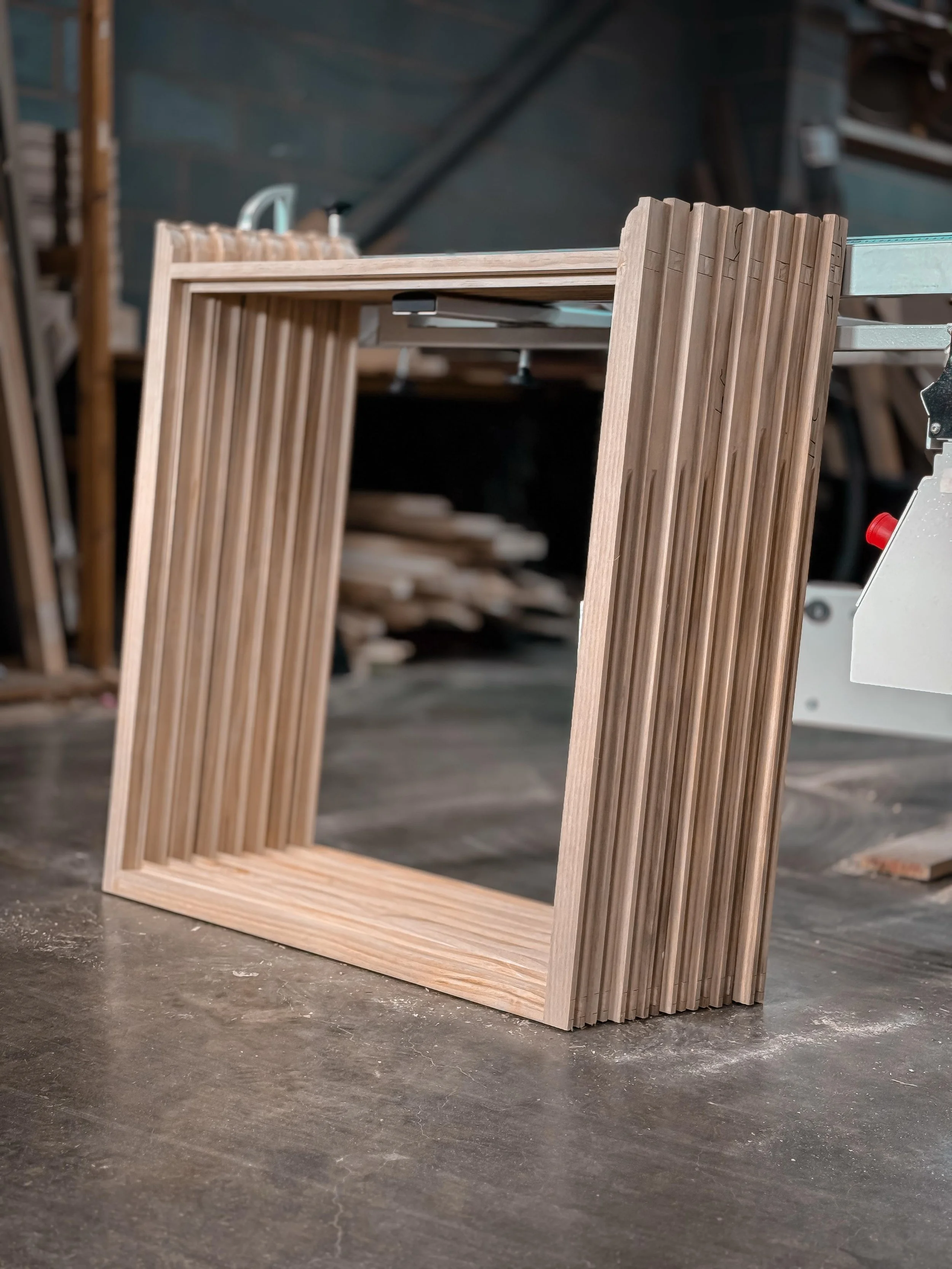 A wooden frame with vertical slats, possibly a piece of furniture or decorative item, on a workbench in a woodworking shop. handmade bespoke accoya