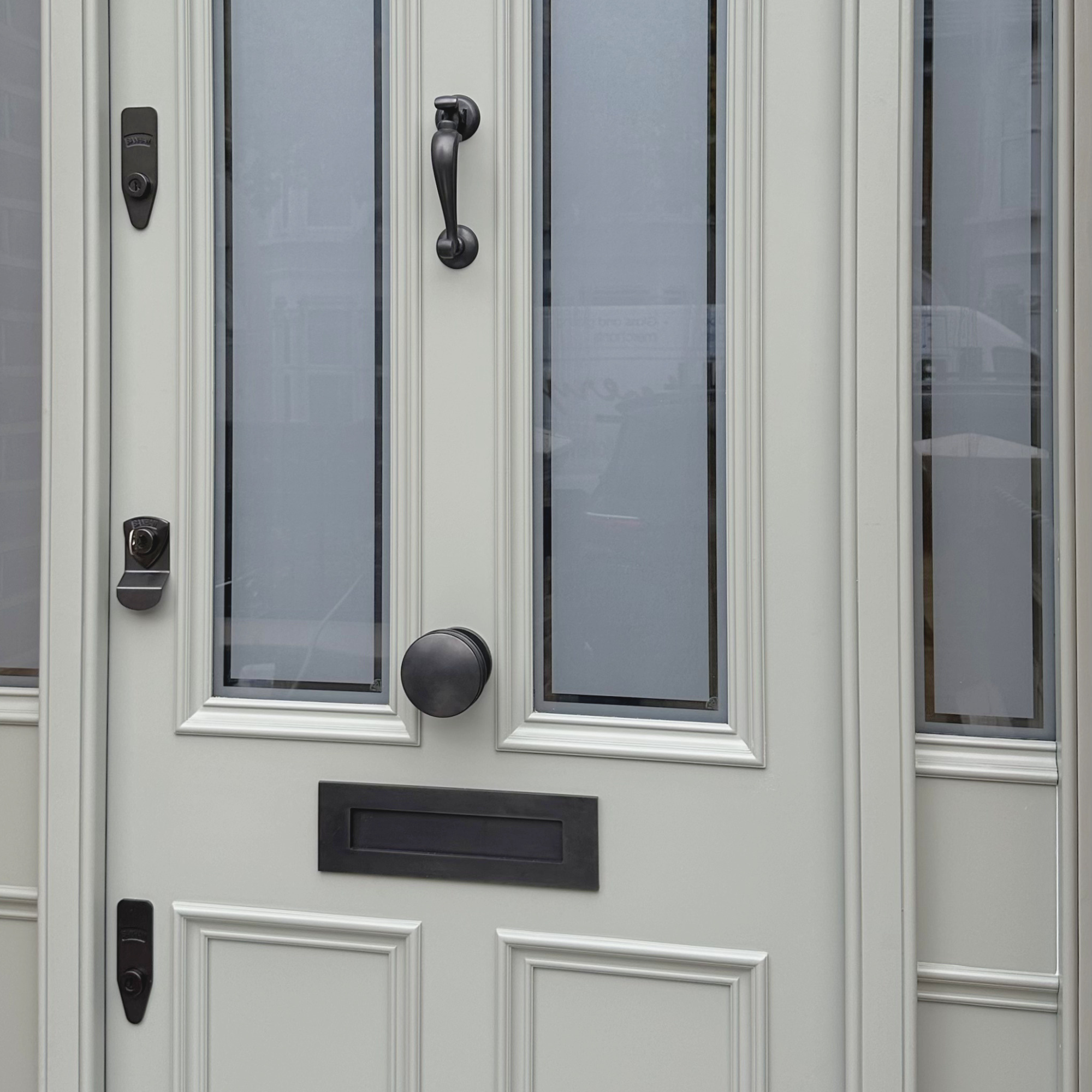 Close-up of a white front door with decorative molding, glass panels, a black handle, and black hardware including a keypad lock and doorbell. handmade bespoke accoya door.
