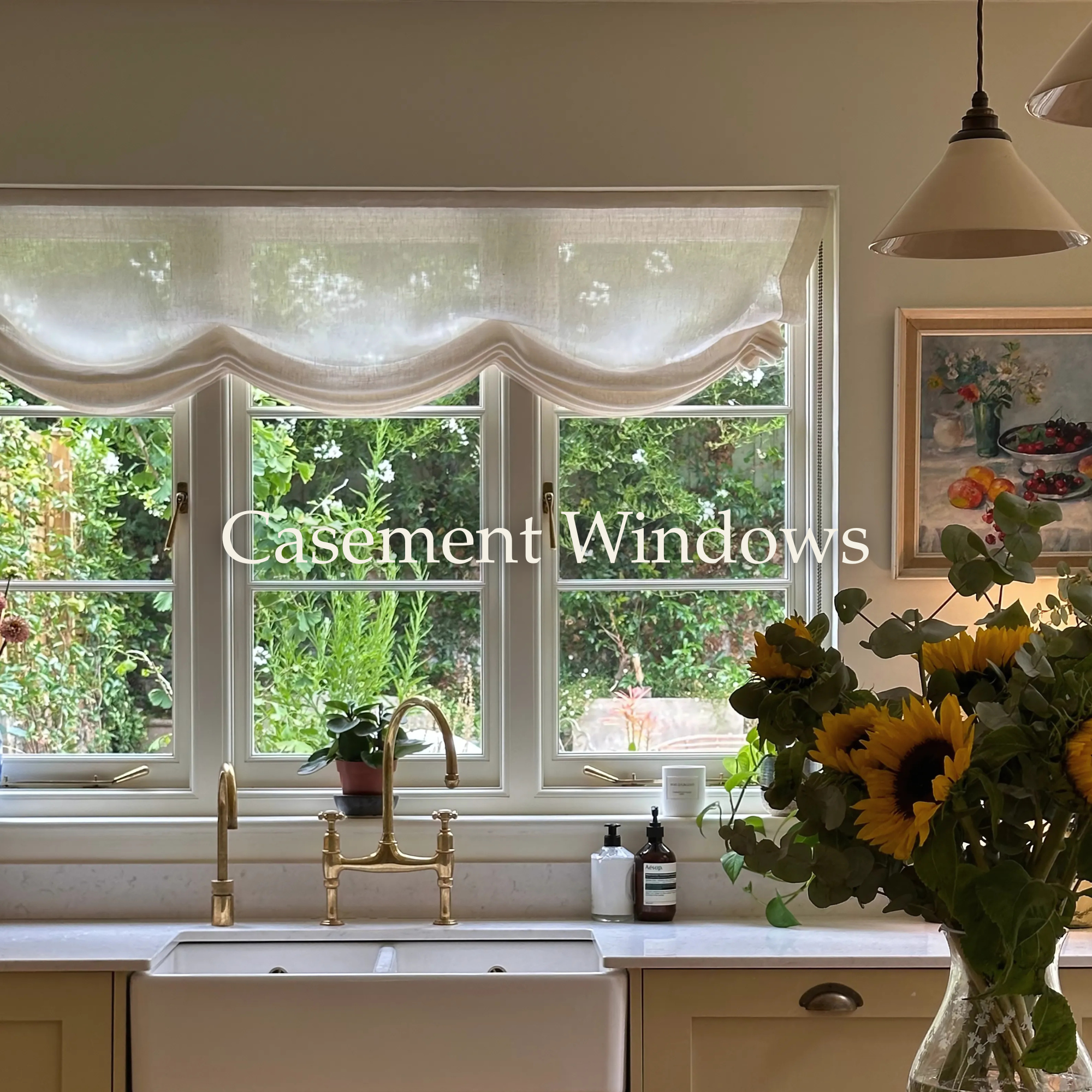 Kitchen sink beneath a large window with floral curtain, sunflowers in a vase on the countertop, and plants outside visible through the window.