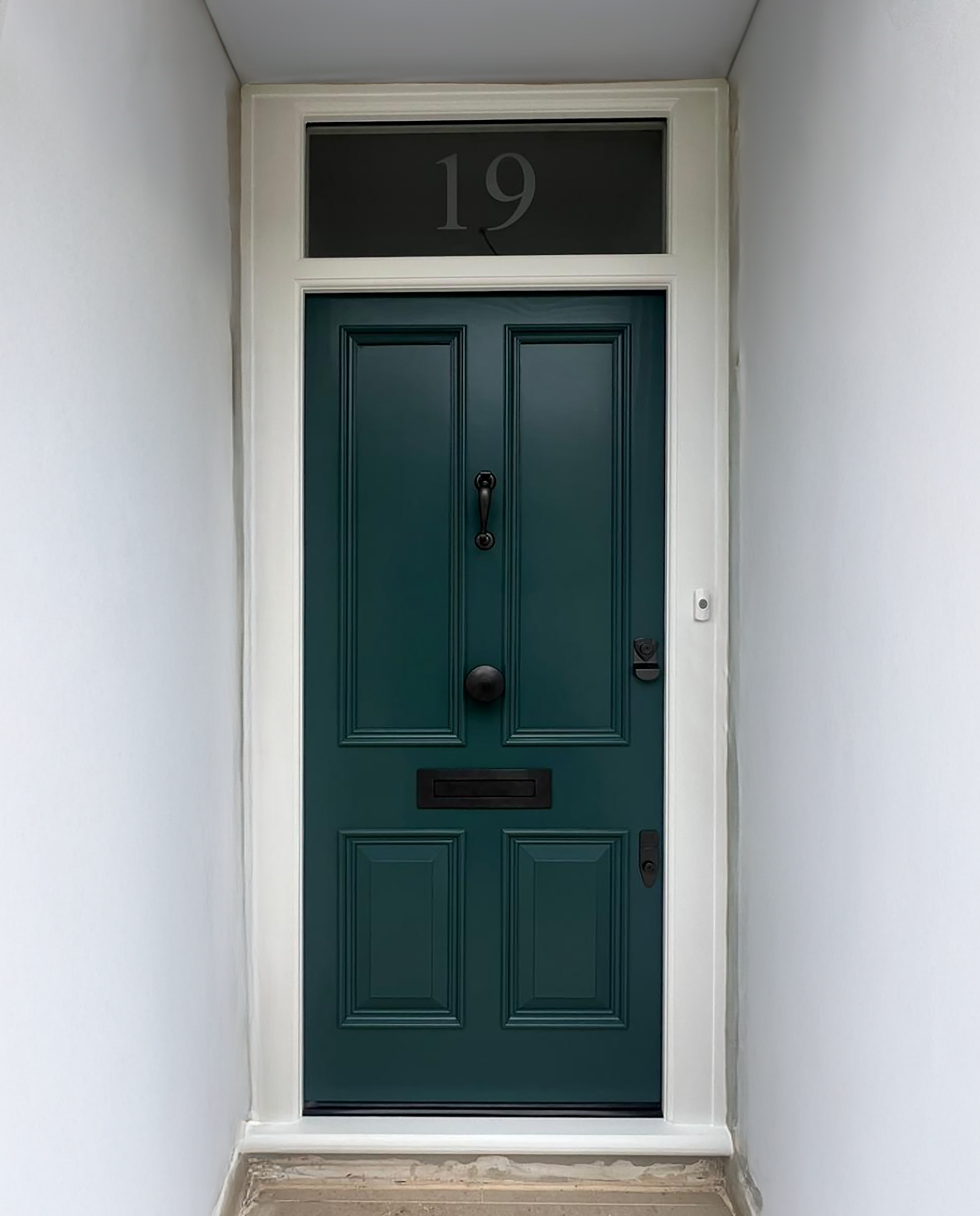 Front door painted dark teal with a black door handle, letterbox, and a doorbell on right side. House number 19 displayed in glass panel above the door. handmade bespoke accoya door.