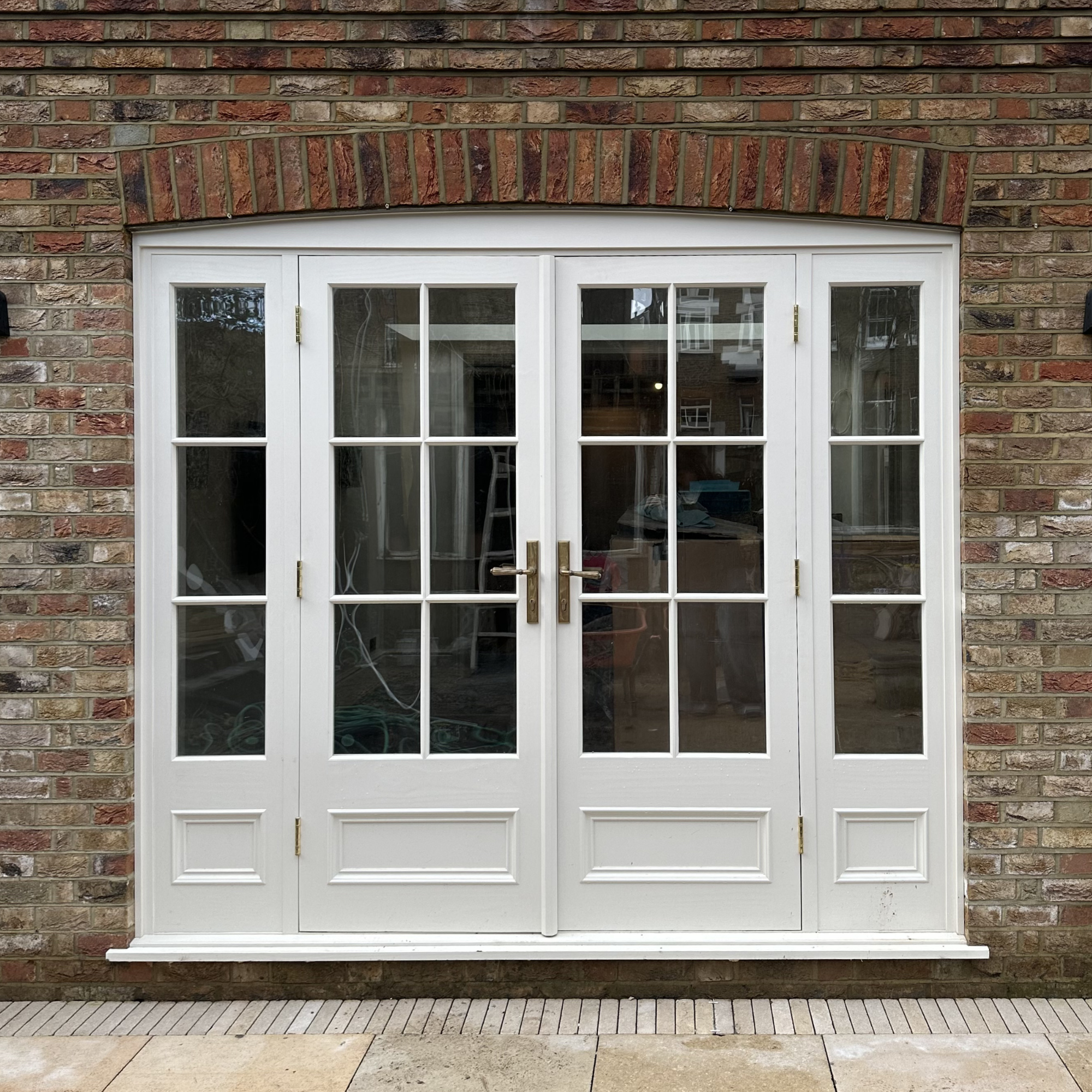 White handmade bespoke accoya door. French doors with glass panes leading outside, set in a red brick wall.