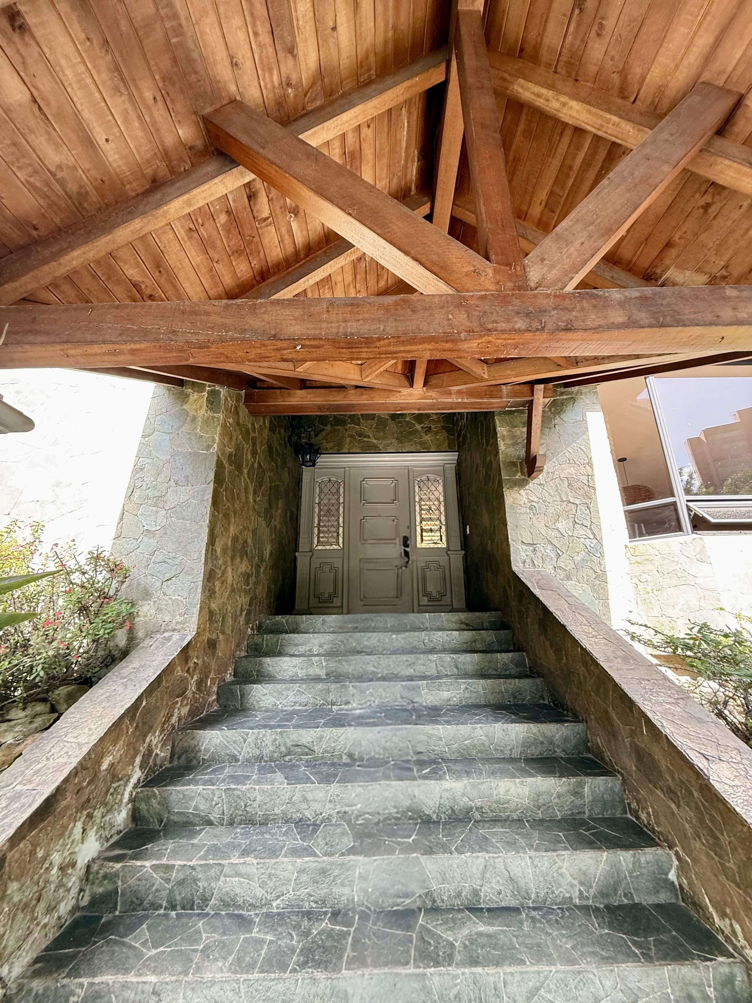 Stone staircase leading up to a door at an exterior entrance with a stone wall on each side and greenery around.