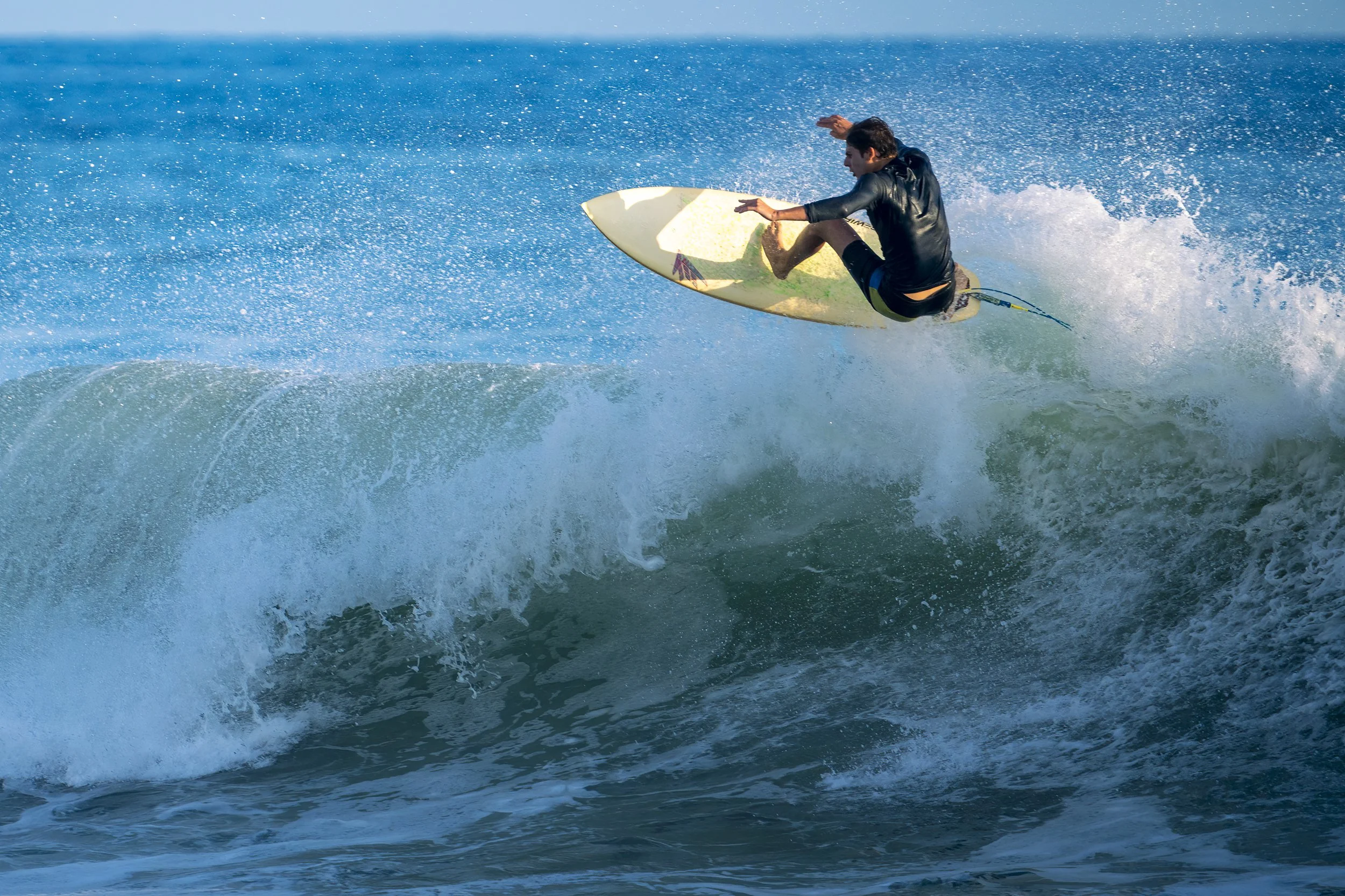 A man surfing on a wave in the ocean, wearing a black wetsuit, and riding a yellow surfboard.
