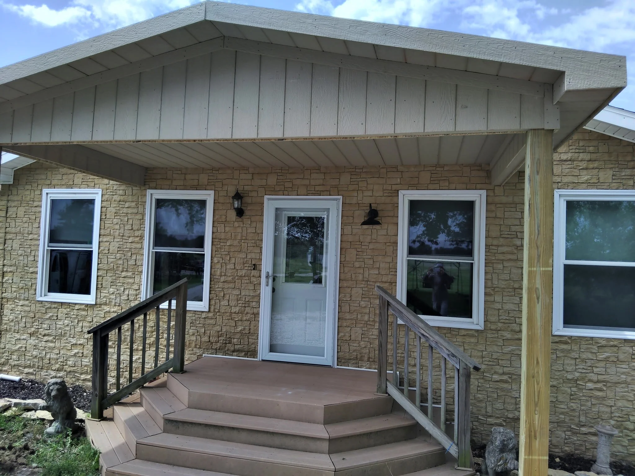 Front porch with stairs leading up to a door, stone wall exterior, three windows, and outdoor lighting fixtures.