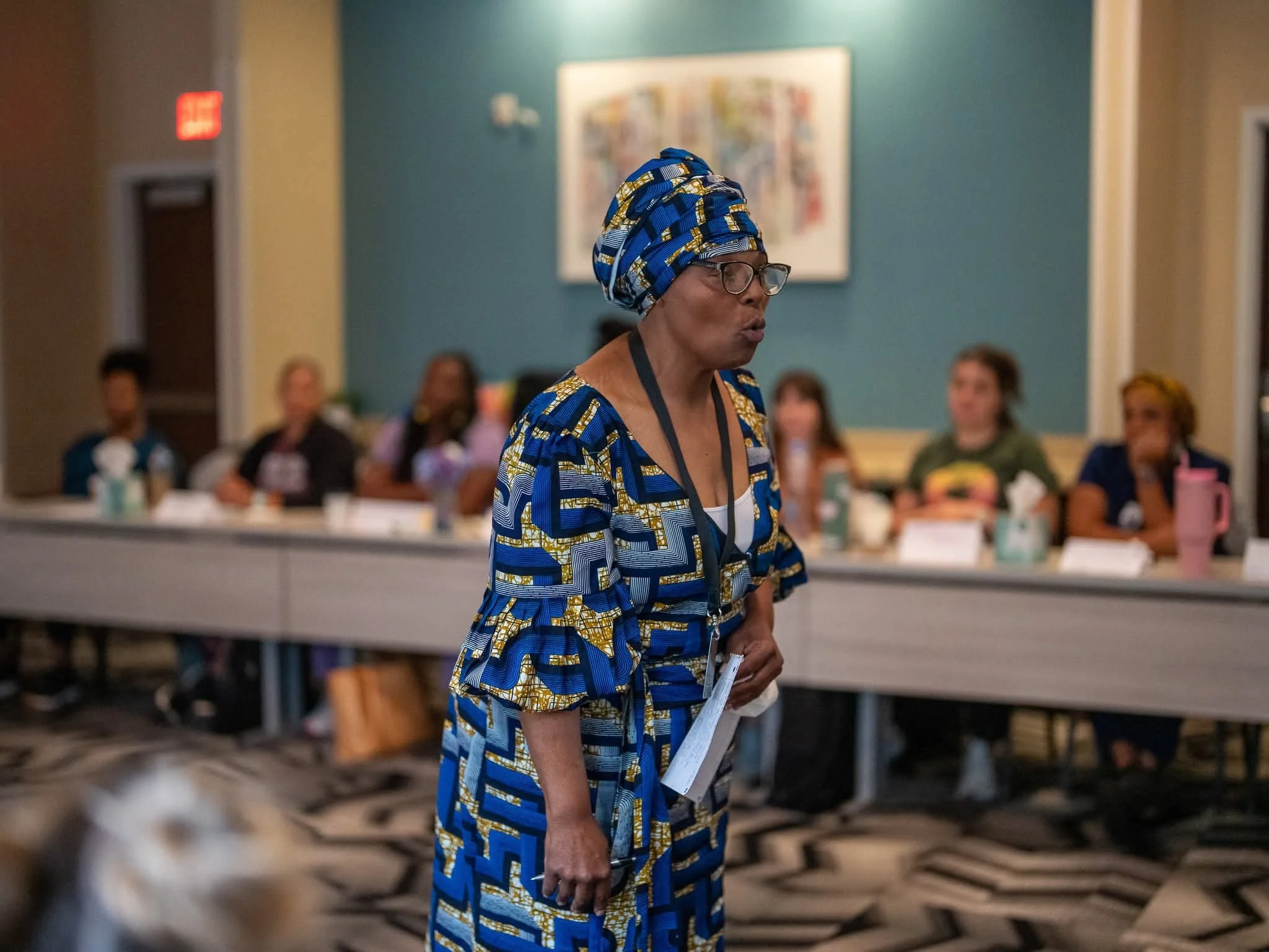 Elder Charlotte Marie Shilo-Goudeau addressing doula training participants while wearing a blue and gold Ankara dress and matching head wrap.