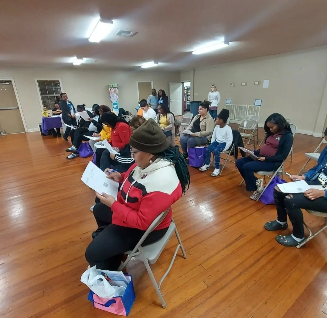 Group of about a dozen people sitting in chairs with paperwork during a childbirth education class.