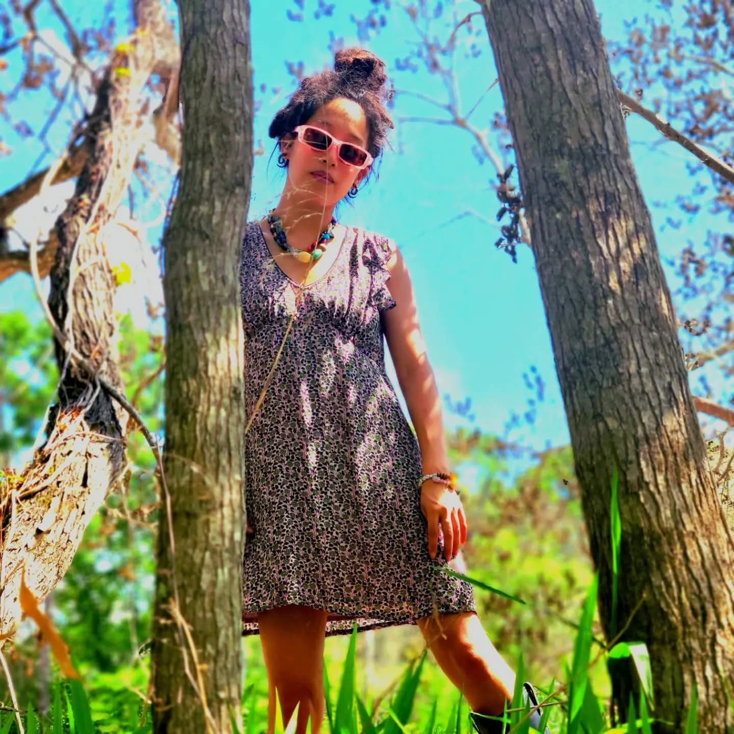 CBC community doula Saeyoung, a black woman, wearing a dress and sunglasses looking town at the camera standing next to a tree.