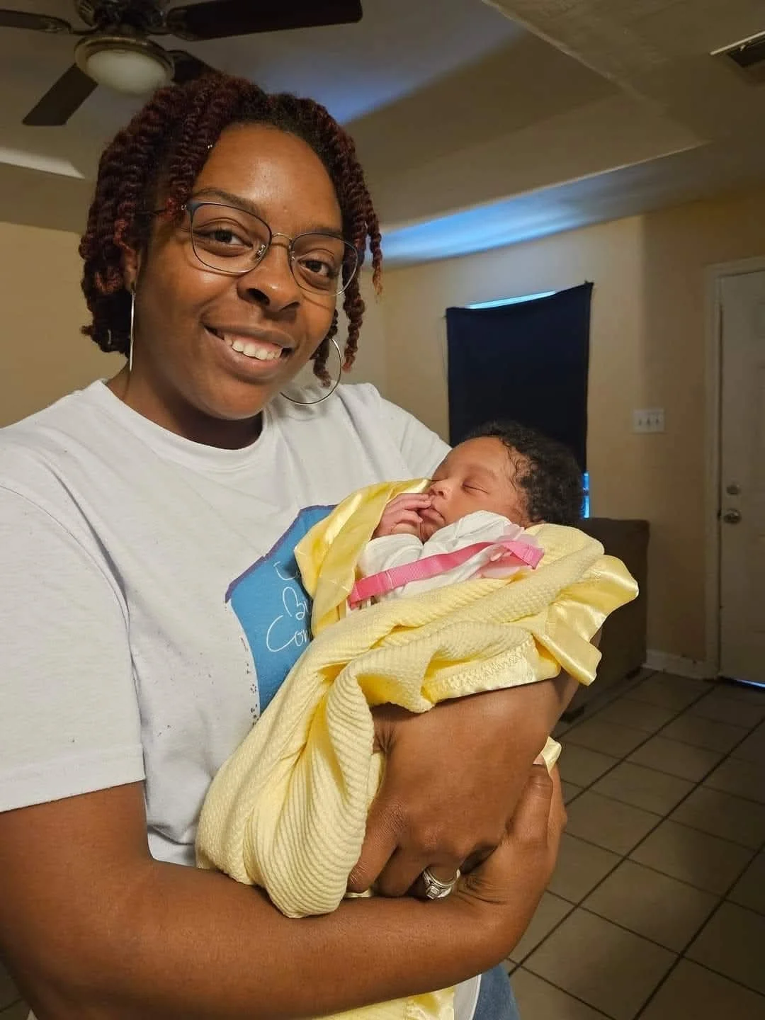 CBC community doula Johnnetta, a Black woman, smiling while cradling a sleeping newborn wrapped in a yellow blanket.