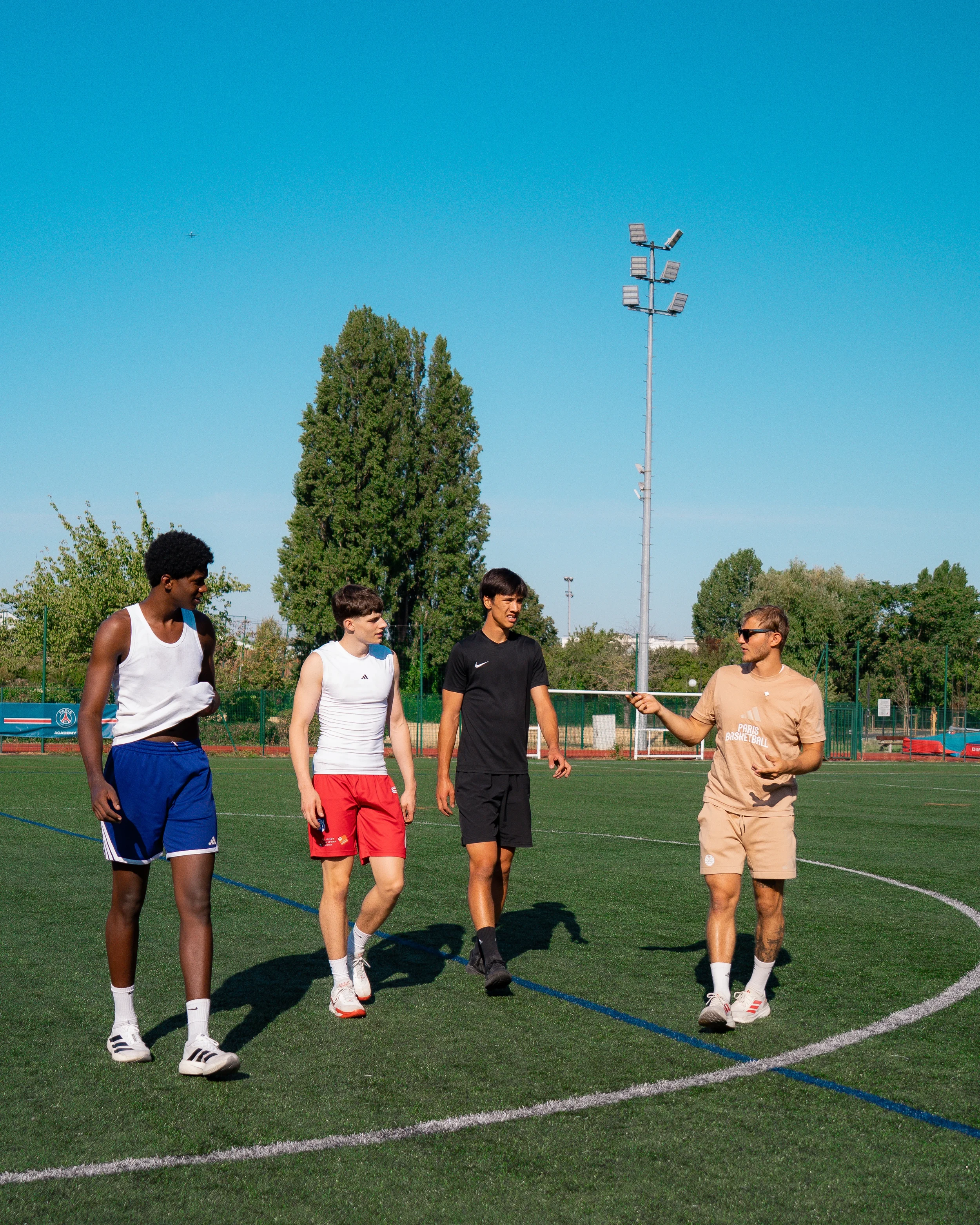 Le coach échange avec trois jeunes sportifs sur un terrain synthétique