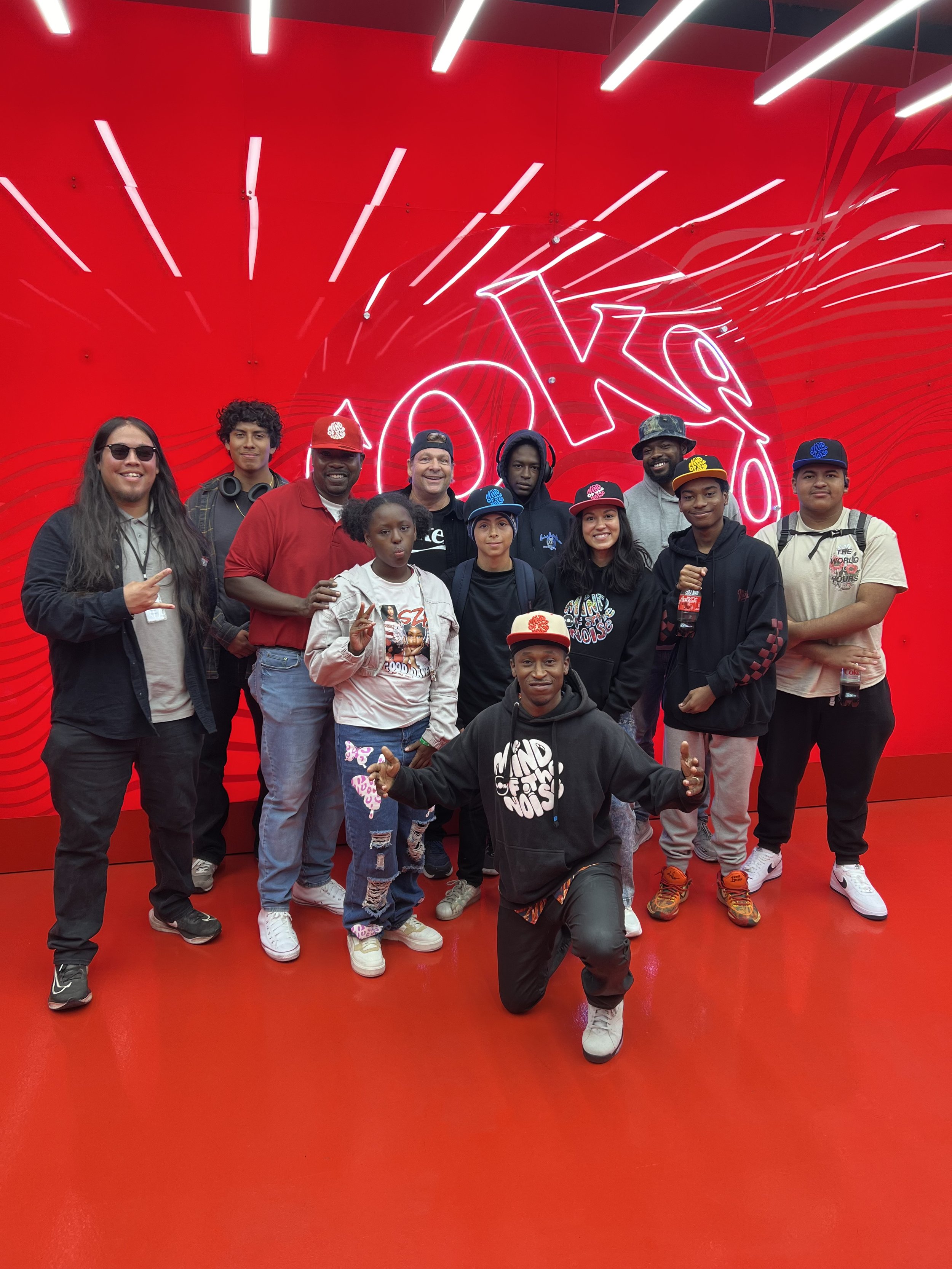 A group of people posing in front of a bright red wall with the word 'JOKER' in neon lights.