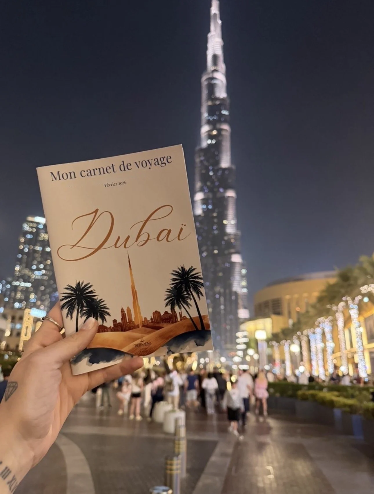 Carnet de voyage personnalisé pour Dubaï, tenu devant le Burj Khalifa illuminé, conçu par Terra Nova Travel Planner pour un séjour sur mesure et optimisé