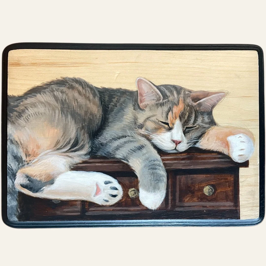 Painting of a sleeping tabby cat lying on a wooden surface with three drawers, with its paws hanging over the edge.