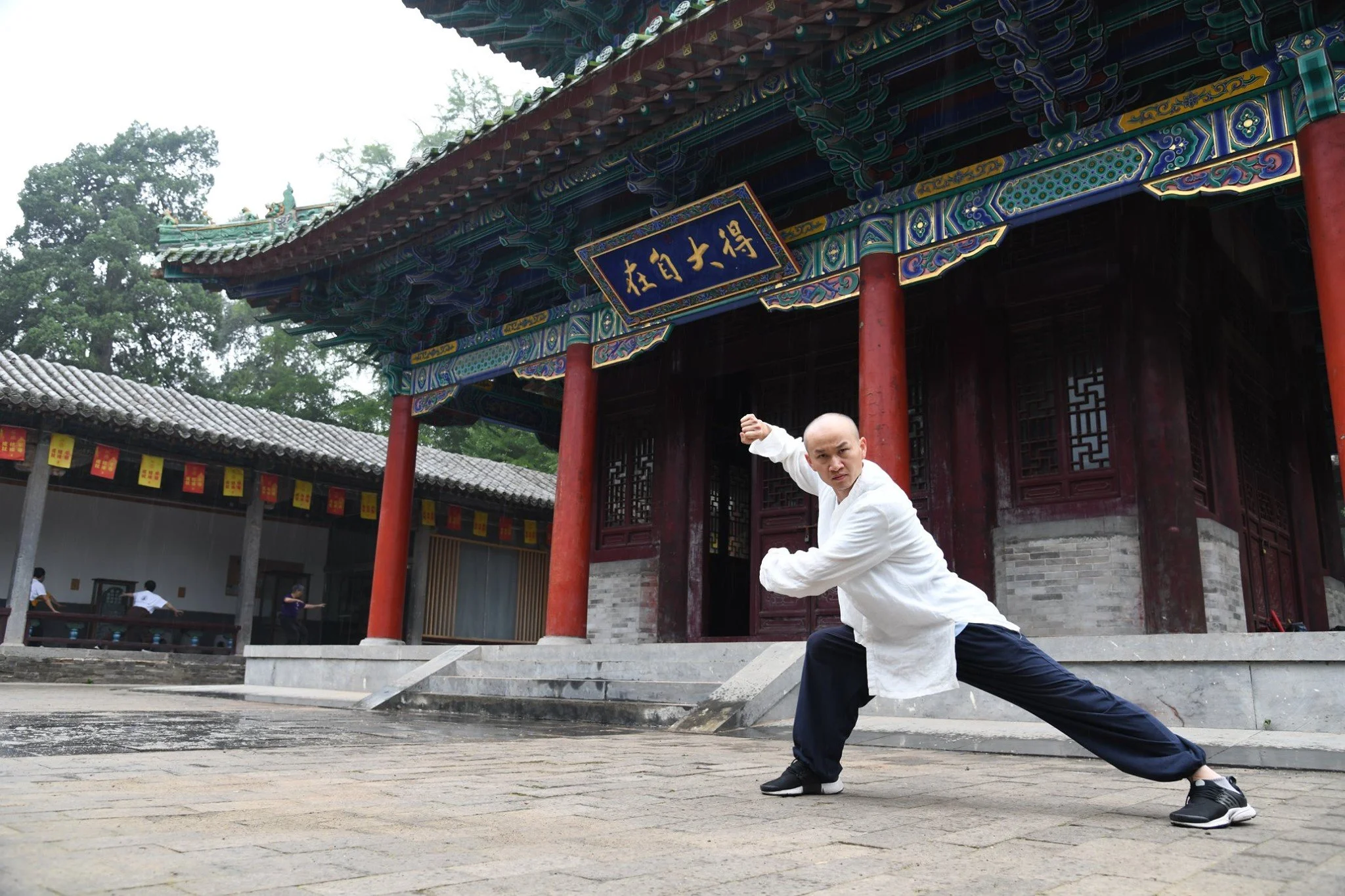 Man practicing martial arts outdoors in traditional Chinese clothing in front of an ornate temple.
