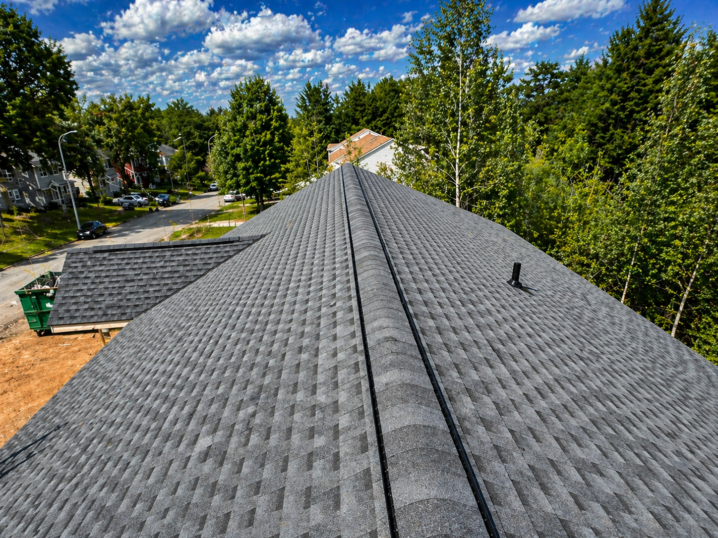 Aerial view of a house roof with gray shingles, black vents, and a blue sky with scattered clouds.