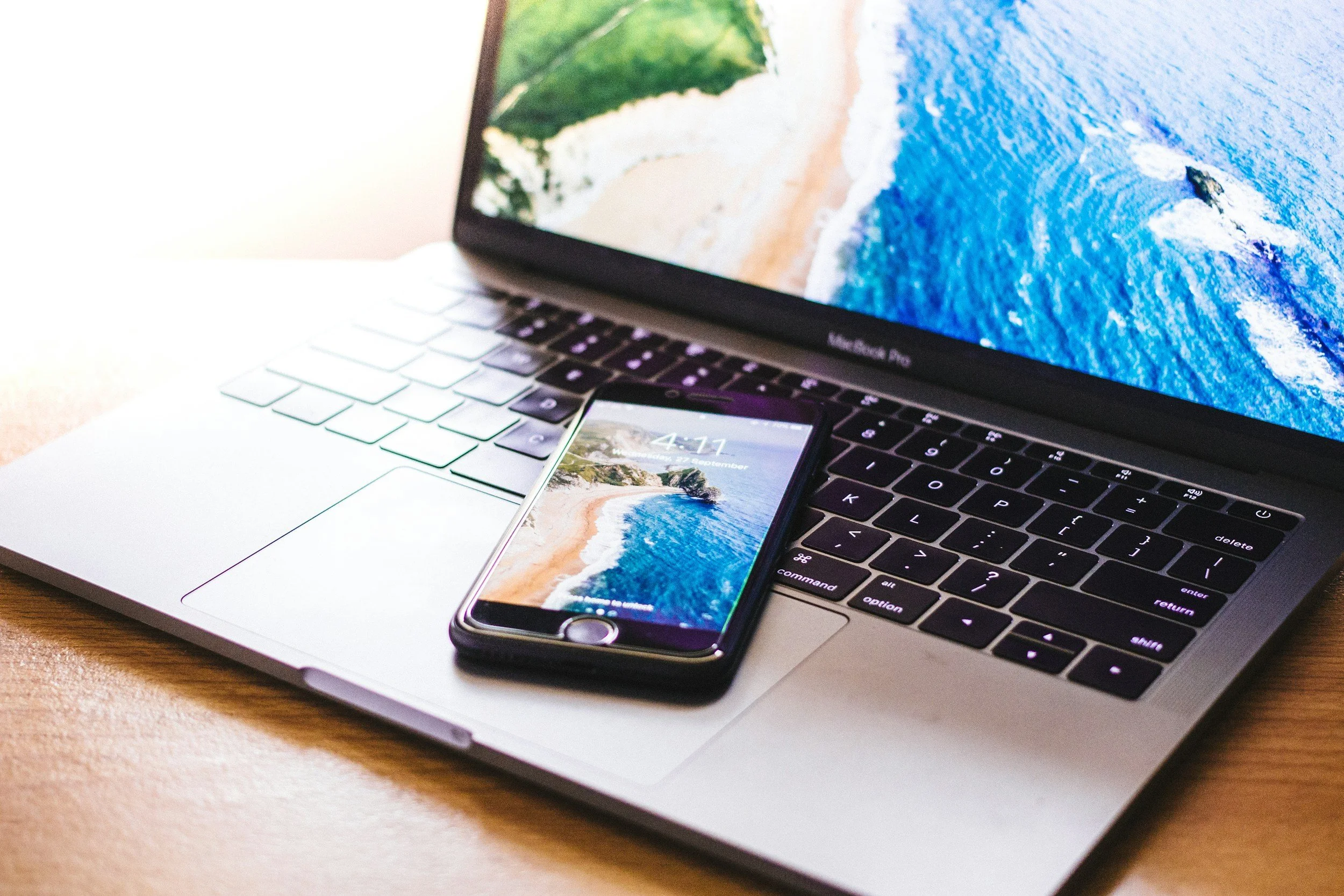Zilveren macbook waar een iphone op light. De schermen tonen zomerbeelden van strand en zee.