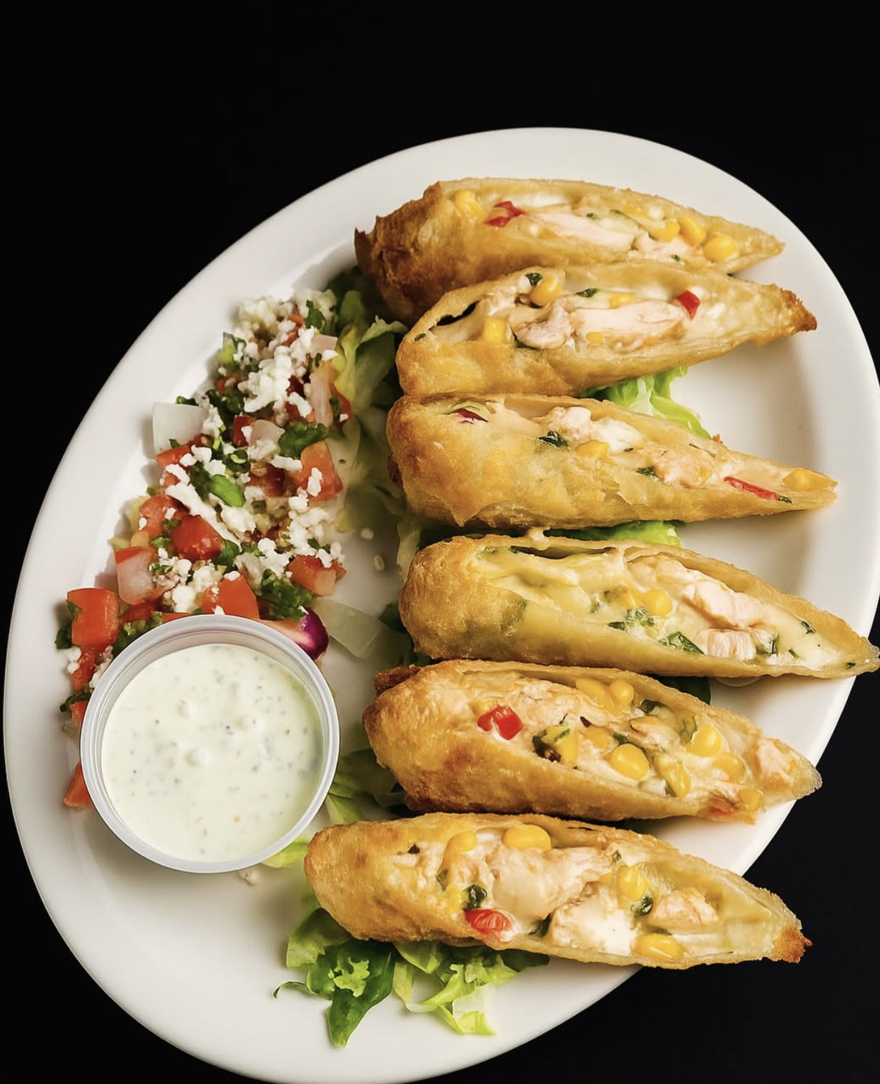 Plate with five stuffed jalapeño poppers filled with chicken, corn, and chopped vegetables, with a side of chopped tomato and onion salad, and a small cup of creamy dipping sauce.