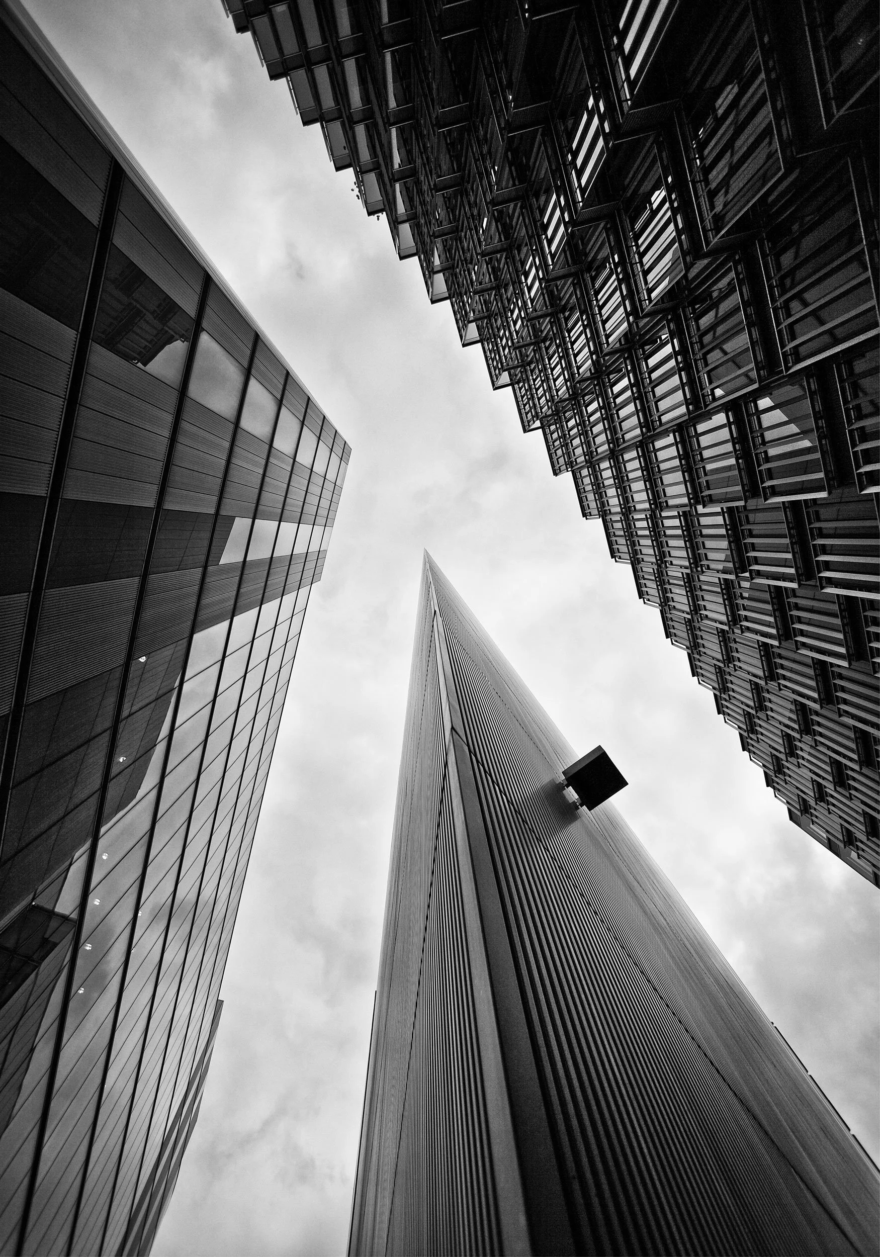 Looking up at tall skyscrapers made of glass and metal, with cloudy sky above.