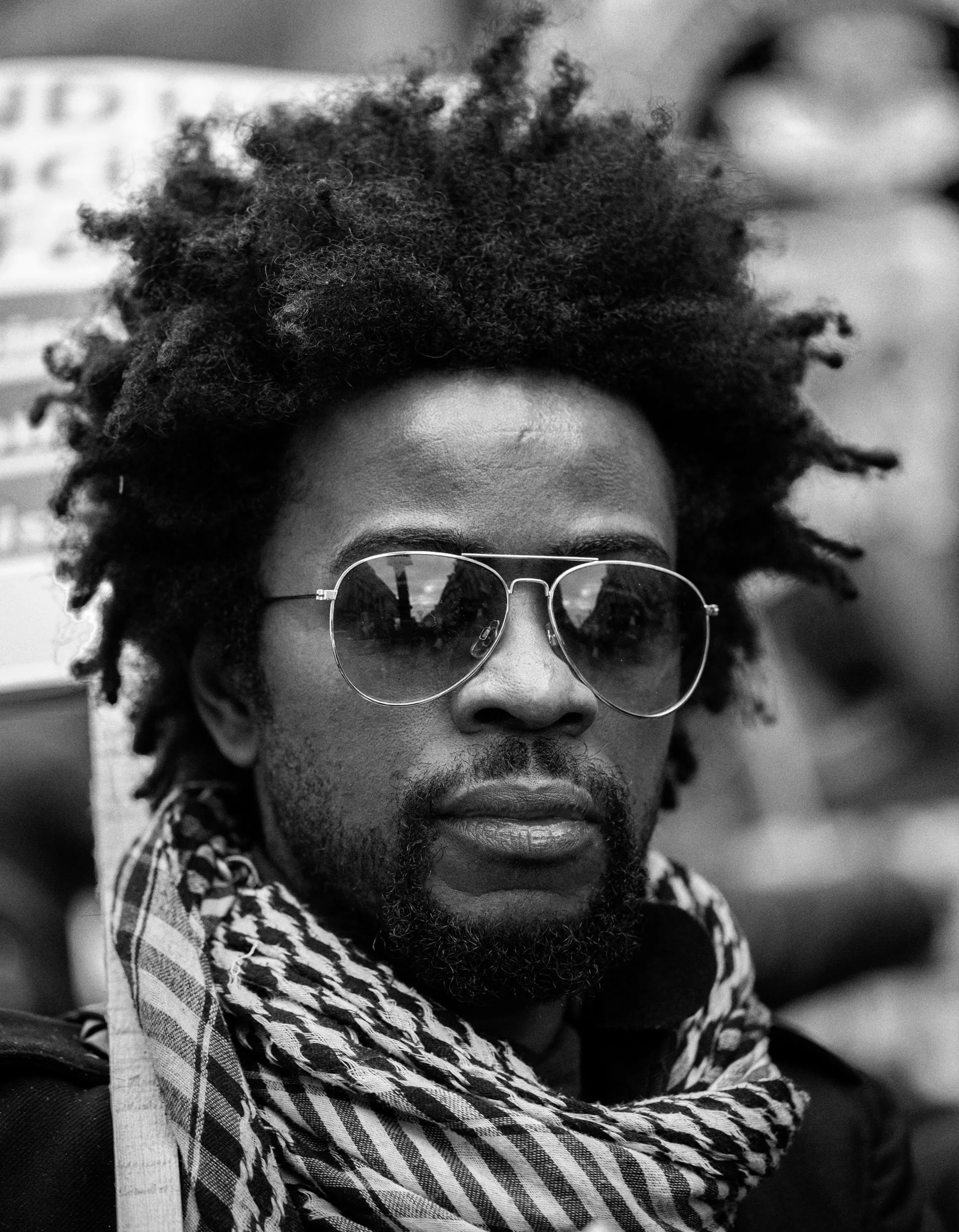 A man with dreadlocks wearing sunglasses and a keffiyeh scarf around his neck.