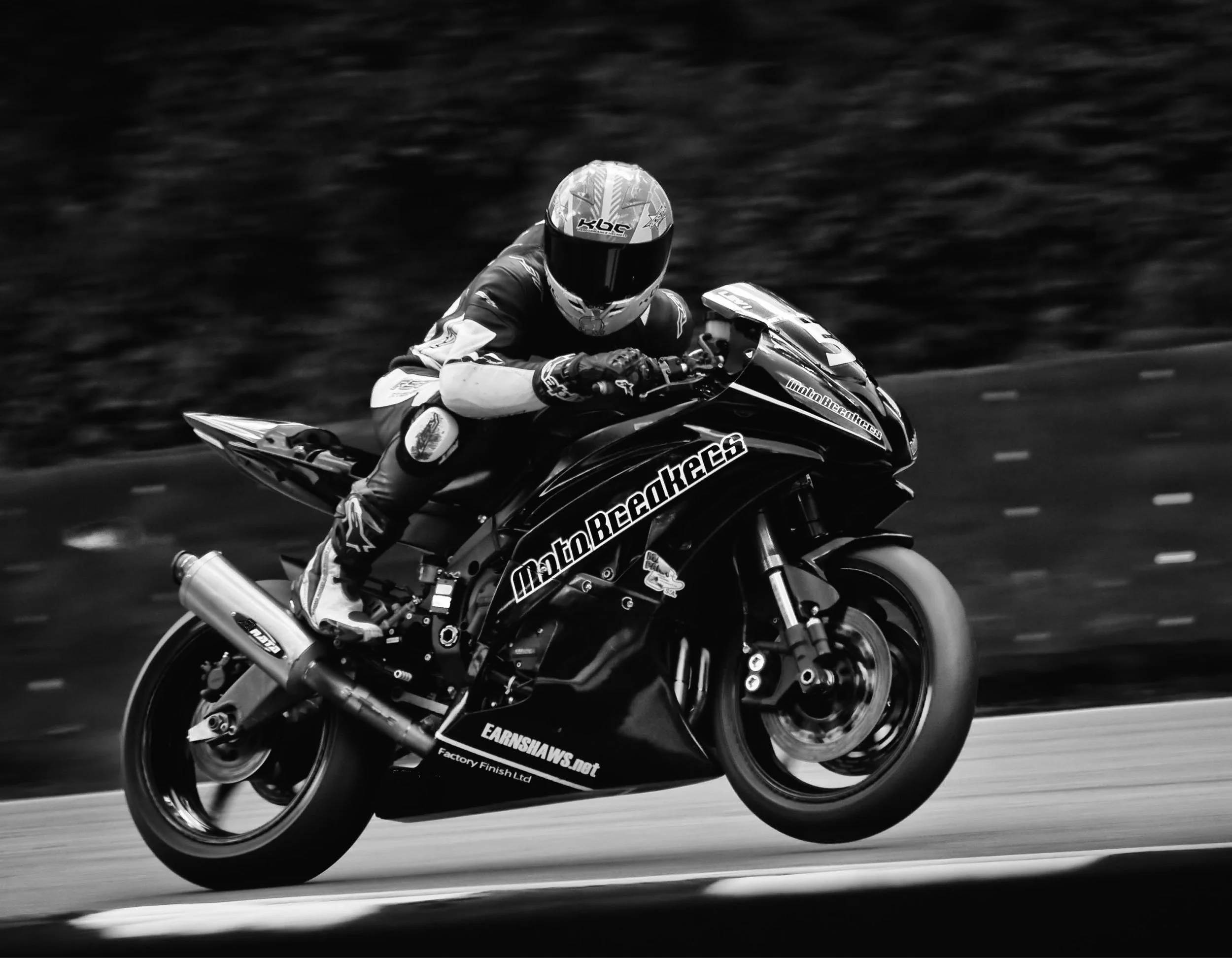 A motorcyclist riding a black sports bike at high speed on a race track, leaning into a turn, with the background blurred to indicate motion.