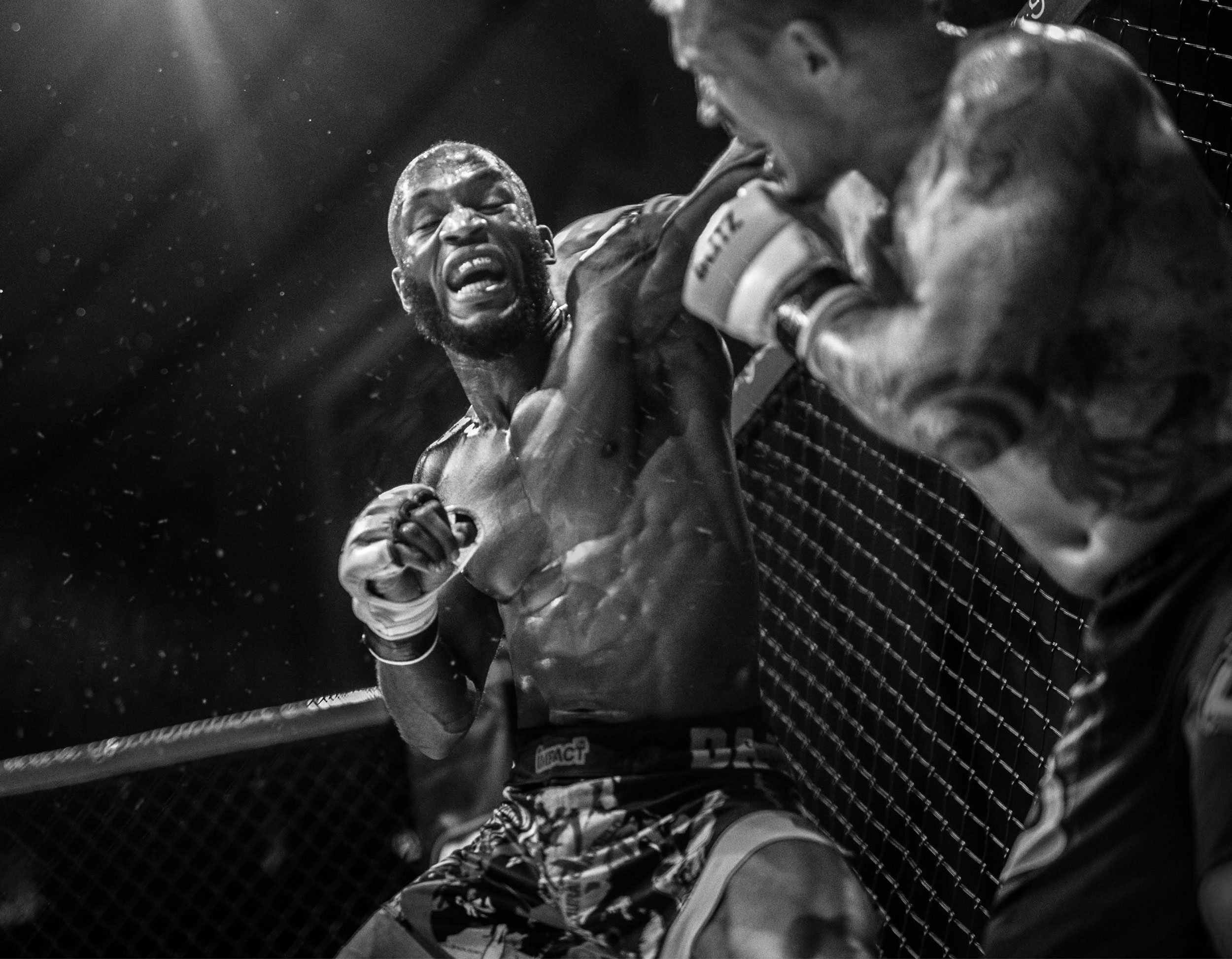 A mixed martial arts fighter in the octagon, looking distressed and exhausted, while another fighter's gloved hand is close to his face.