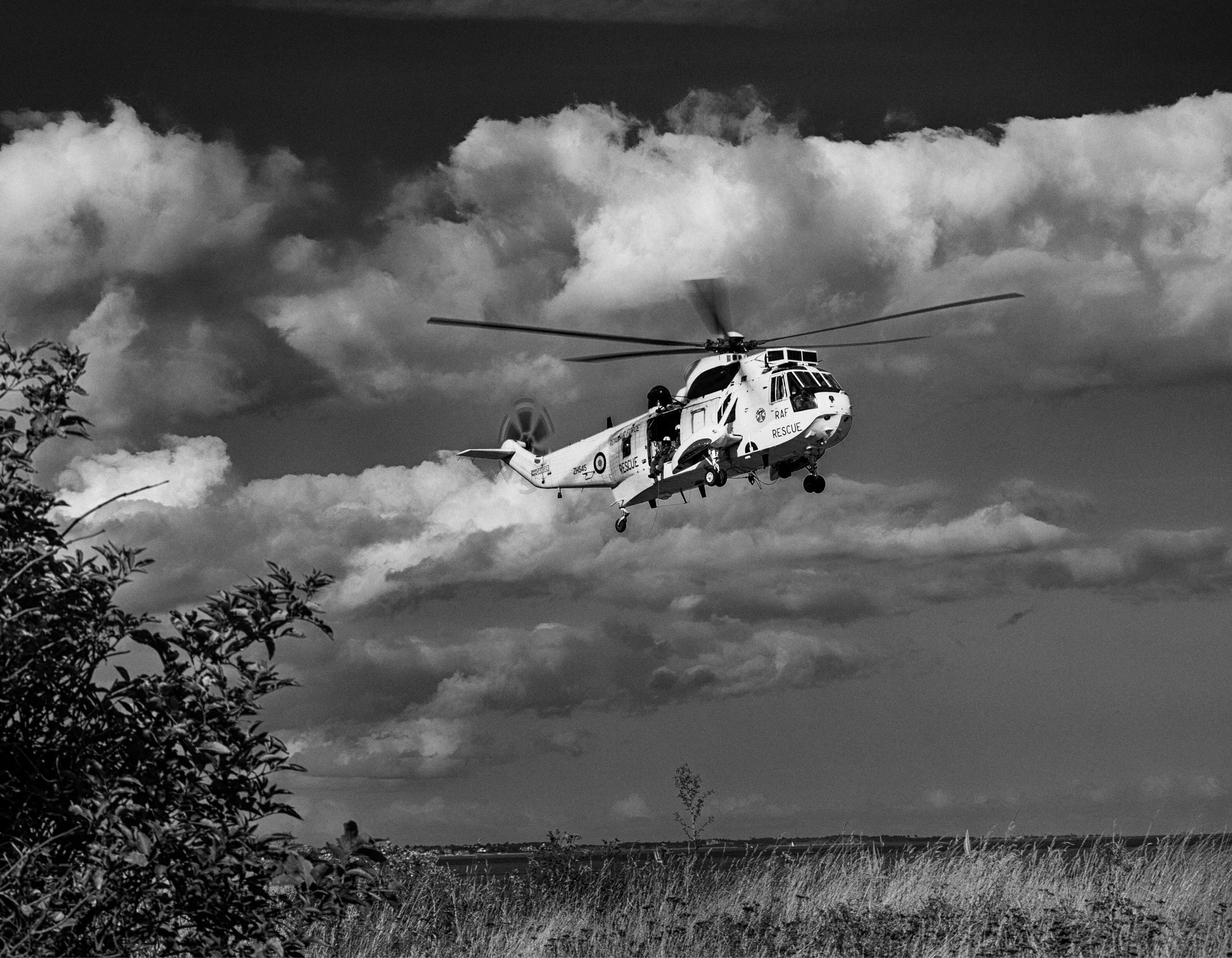 A helicopter labeled 'Rescue' flying over a field with clouds in the sky