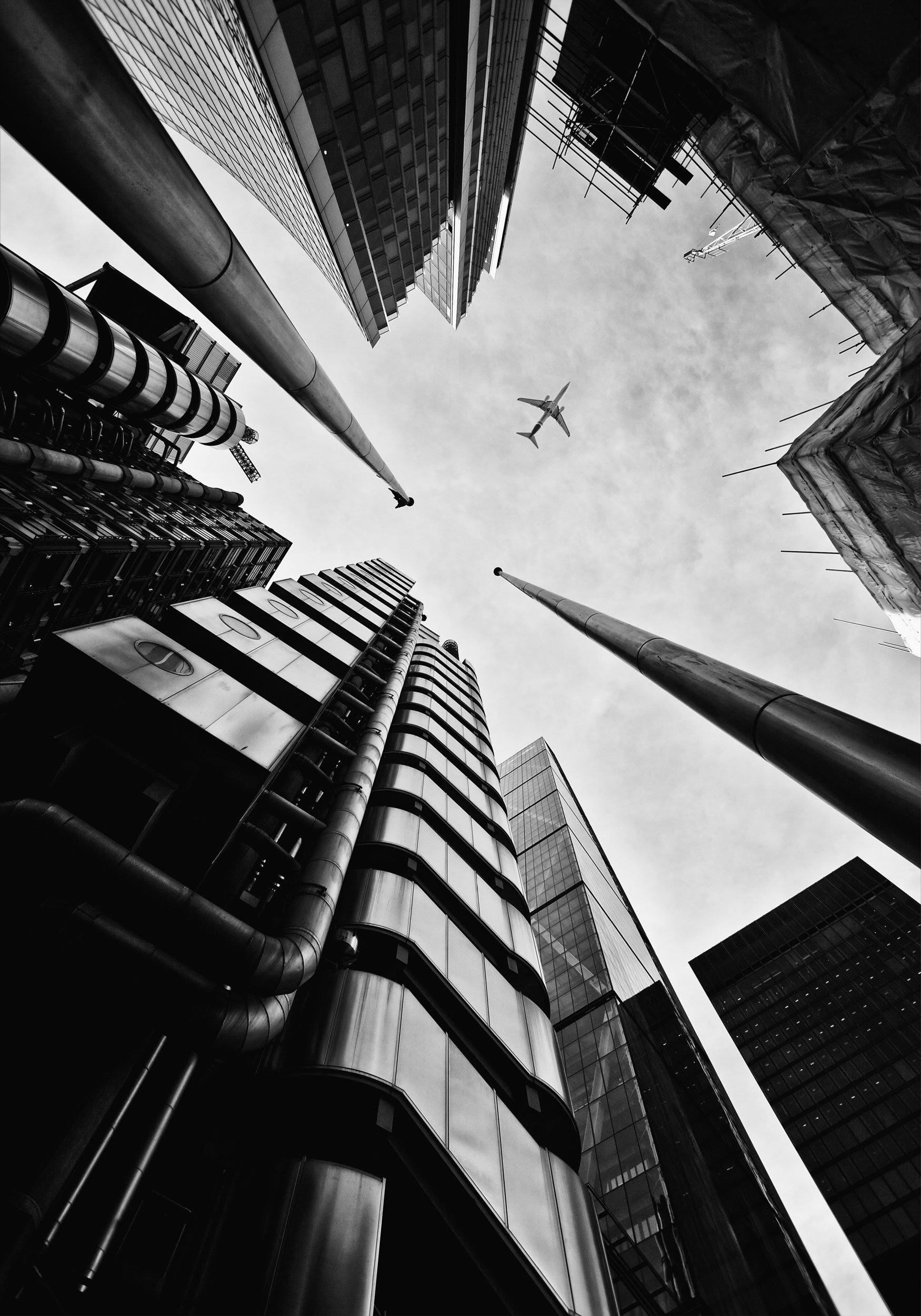 Looking up at tall skyscrapers and buildings in a city, with an airplane flying overhead in the sky.