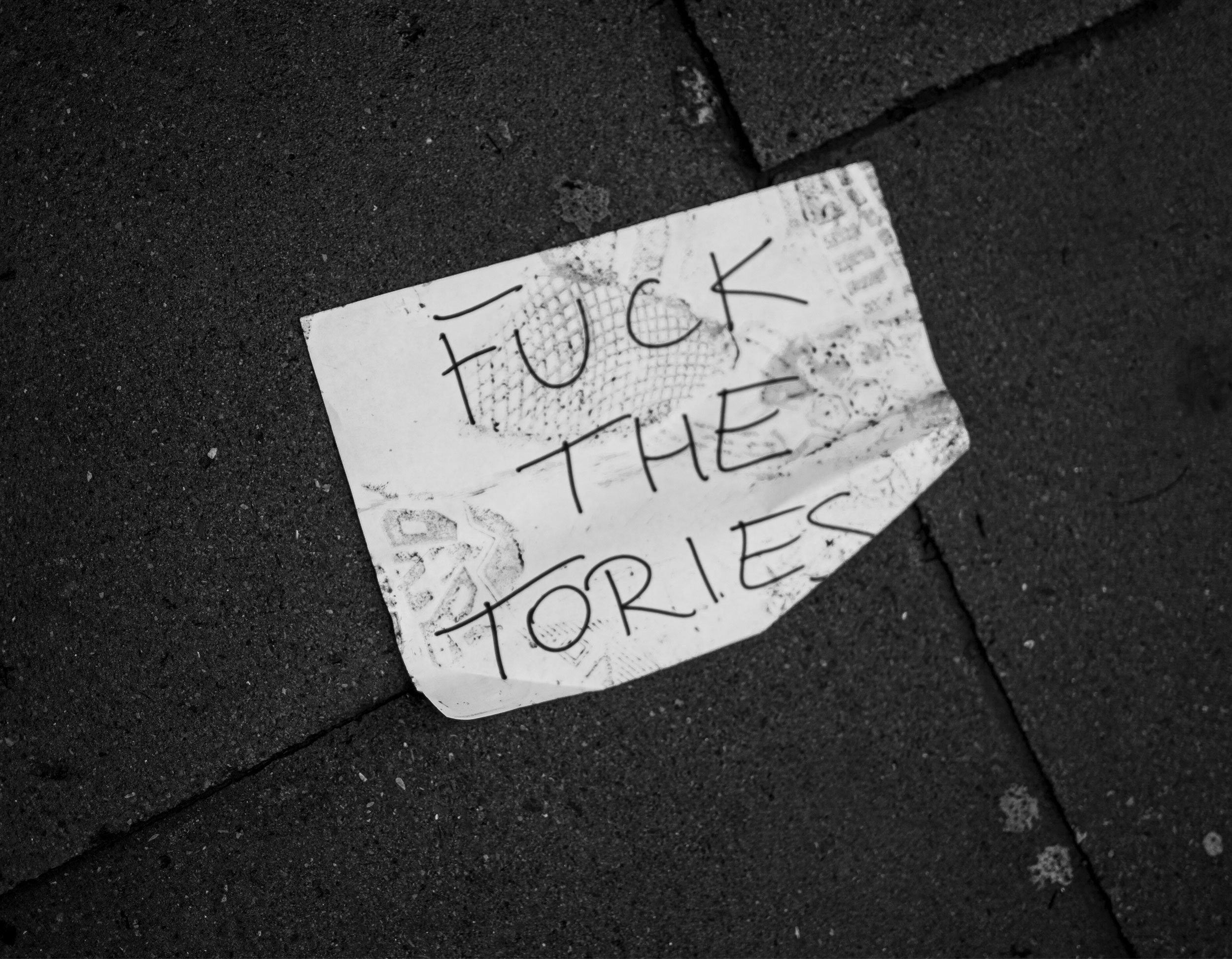 A crumpled paper with the handwritten message "F*** THE TORRIES" on a dark pavement ground.