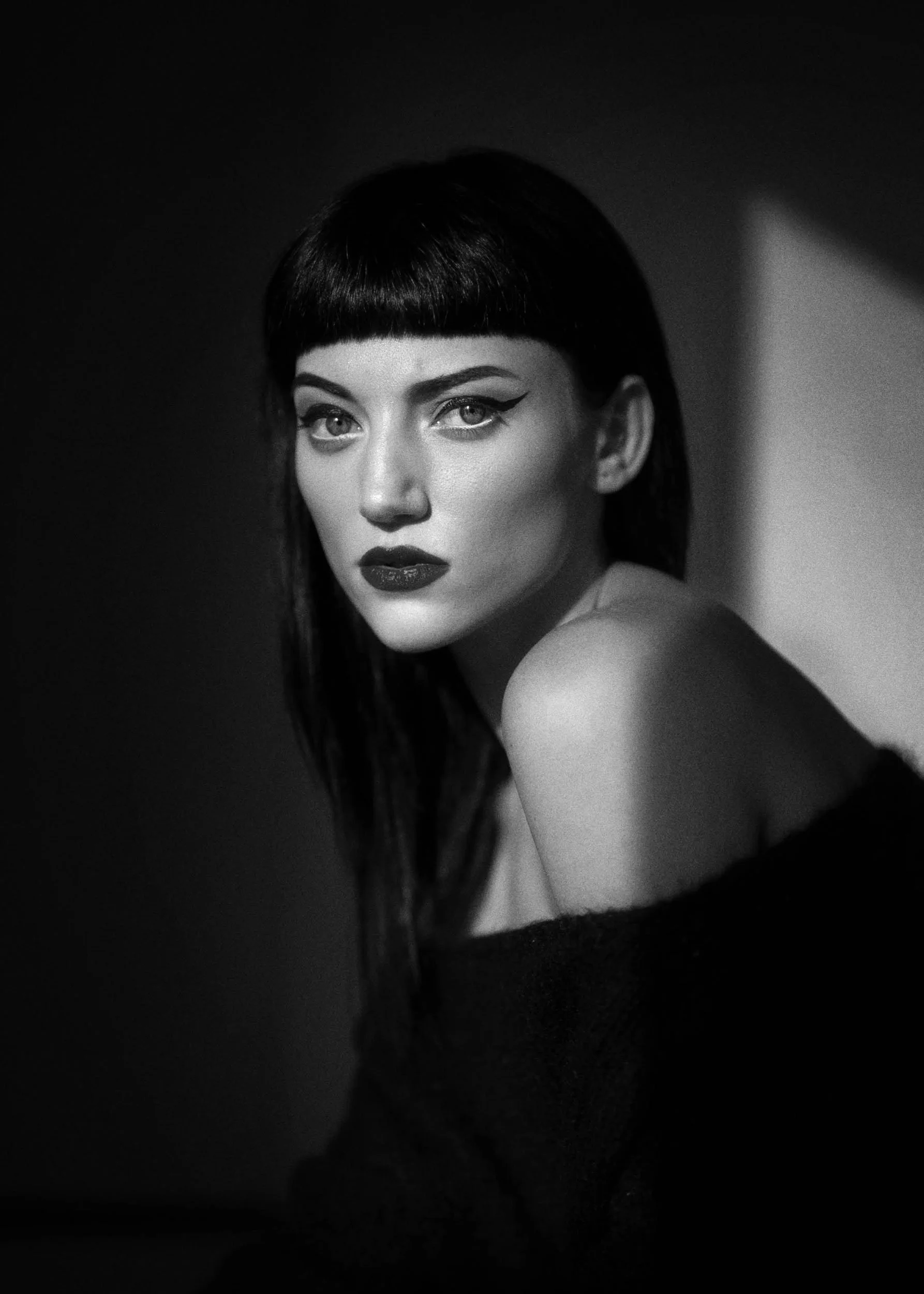 Black and white portrait of a woman with dark hair and bold makeup, looking at the camera with a serious expression.