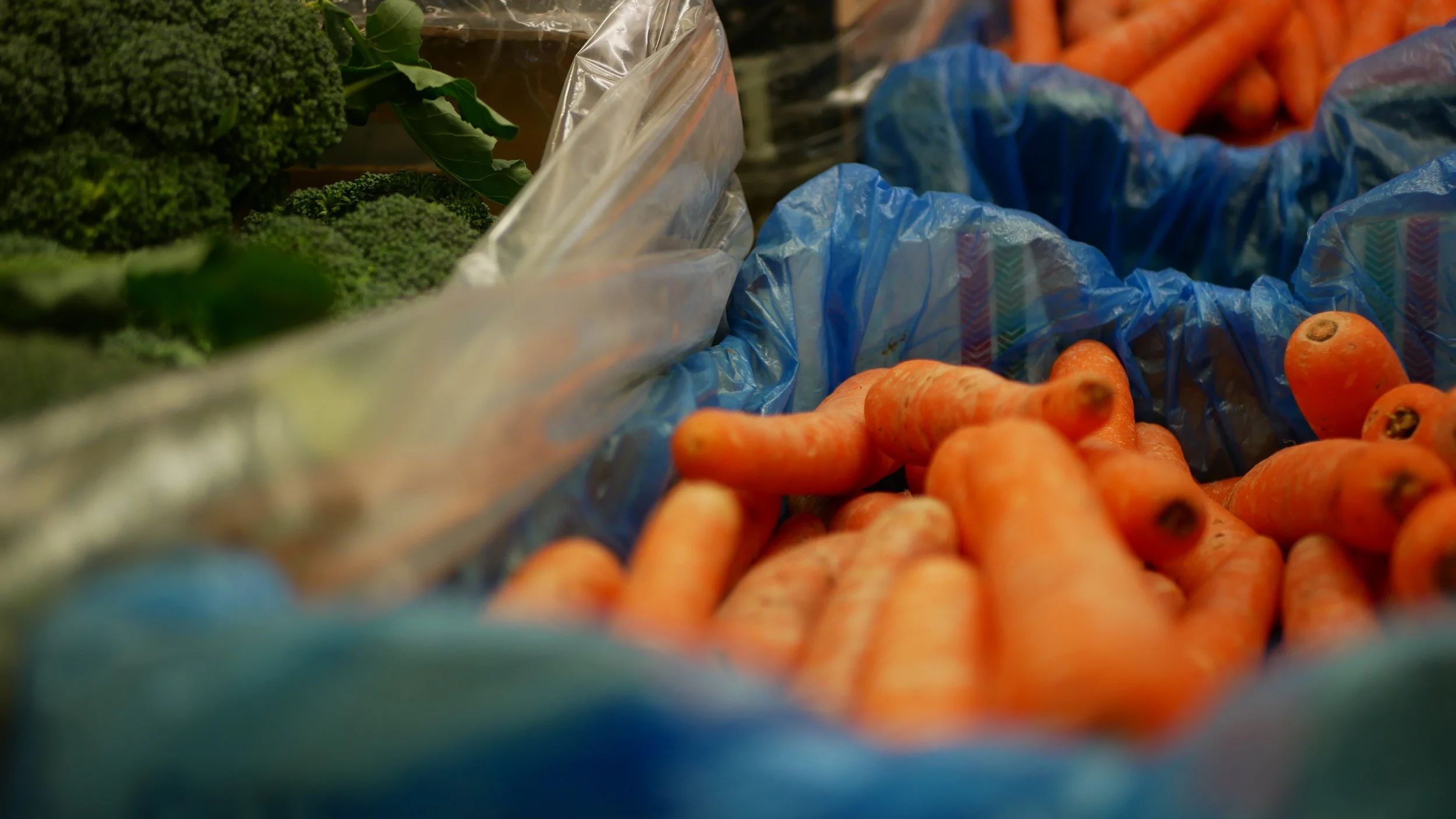 Fresh vegetables including carrots and broccoli in plastic bags at a grocery store.