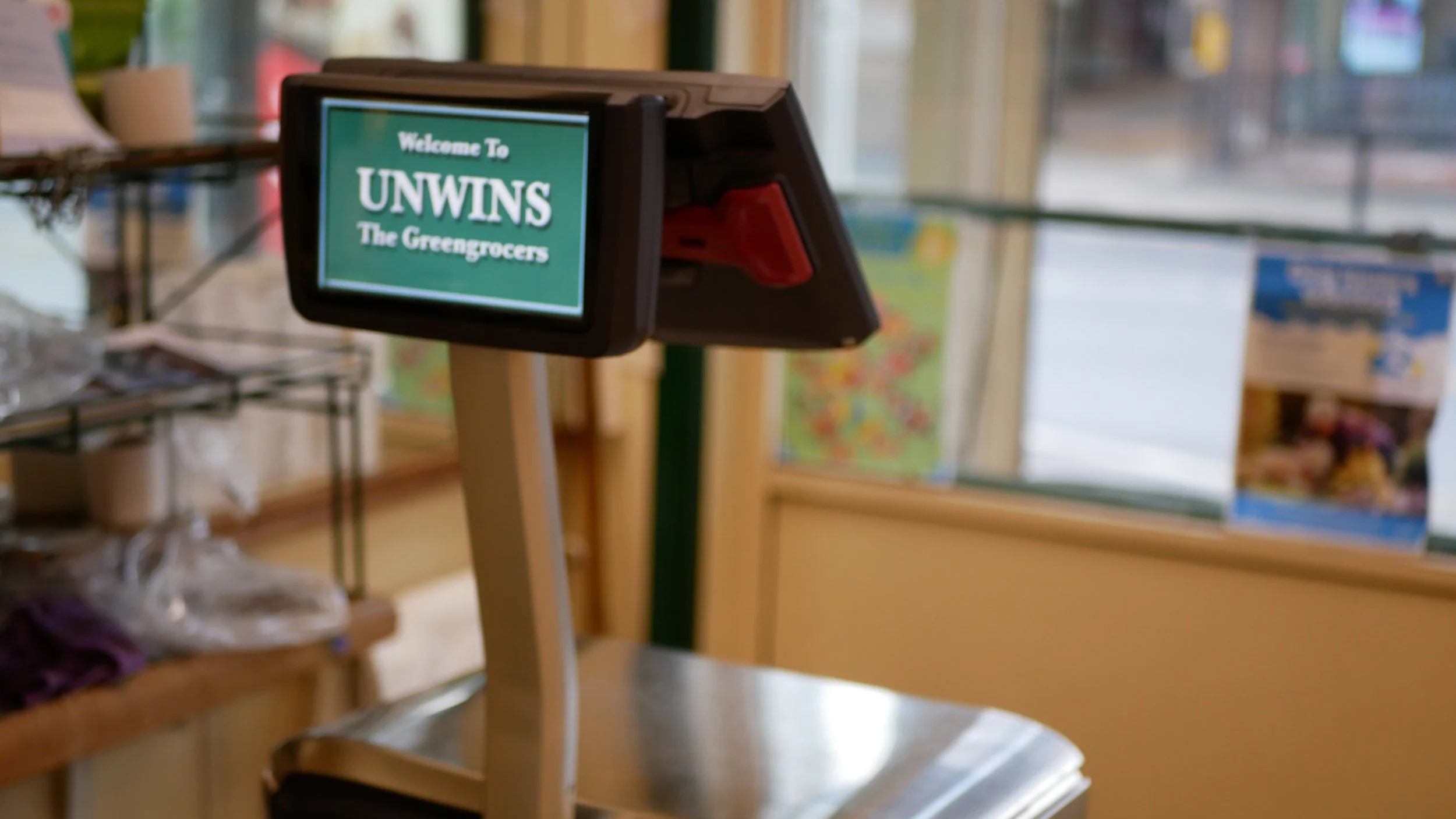 Digital checkout register in a grocery store with a sign that says "Welcome To UNWINS The Grocers".