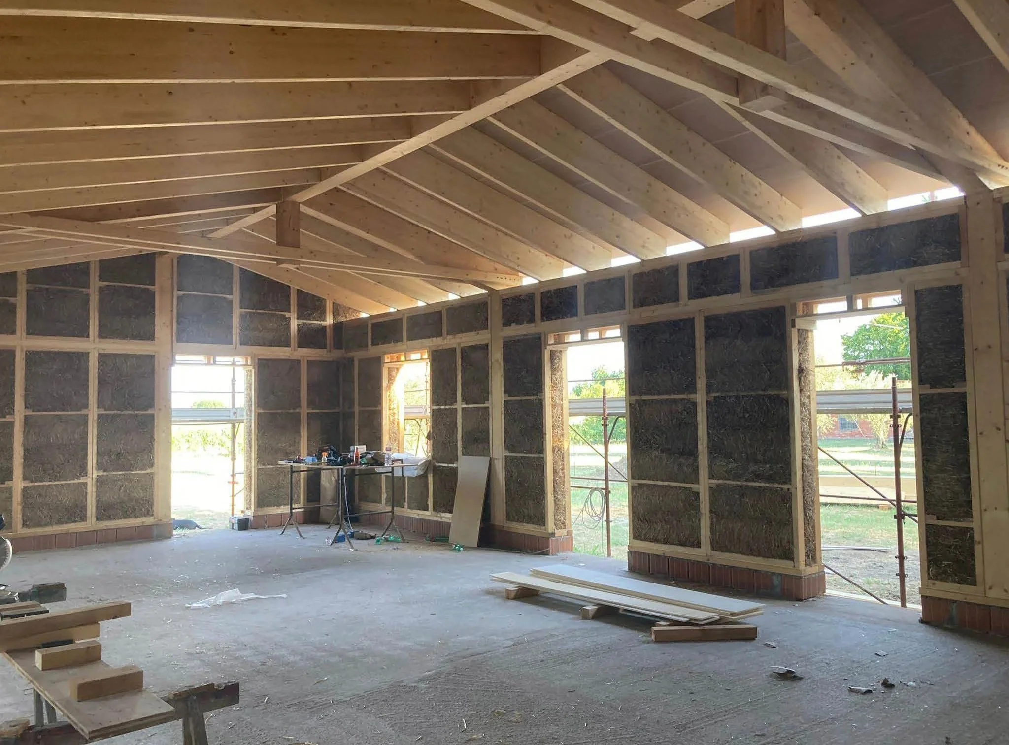 Intervento di costruzione di una casa in legno con struttura a telaio, pareti isolate e soffitto in travi di legno, molte finestre e porte ancora da installare.