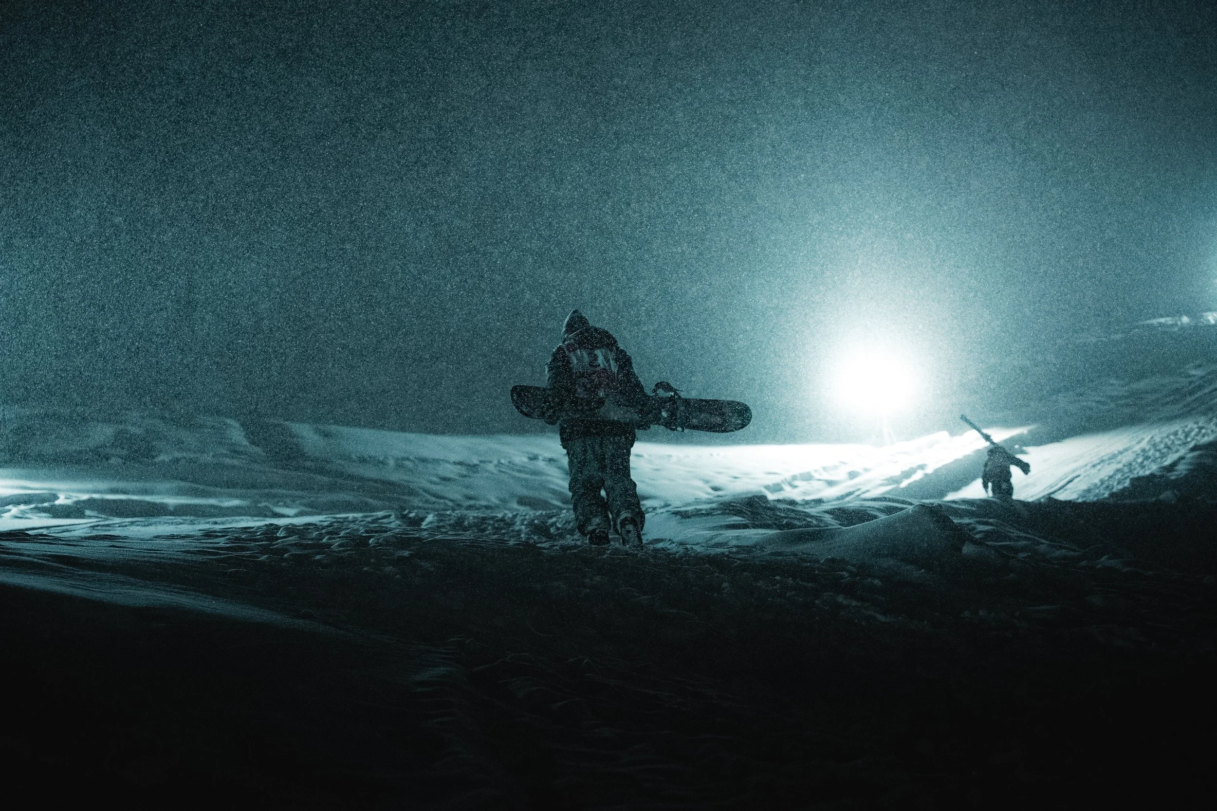 Big Air snowboard contestant walks up the slope at the Whitestyle Open Murren at night under the lights in heavy snowfall