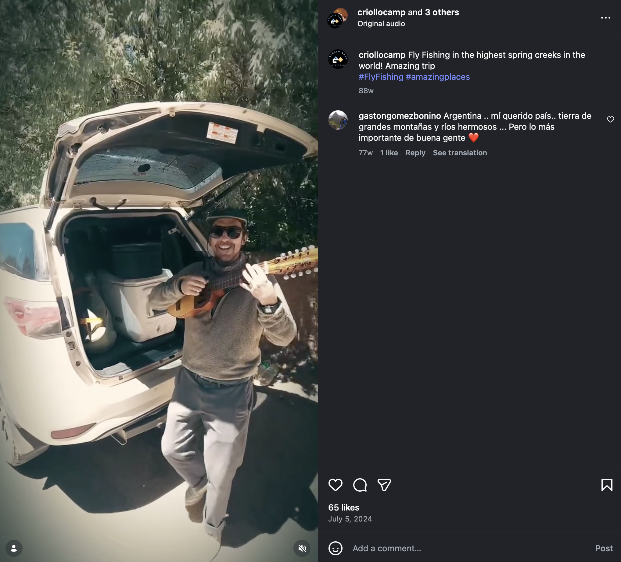 A man wearing sunglasses and a hat standing beside an open trunk of a white SUV, playing a small guitar outdoors amid trees and greenery, smiling at the camera.