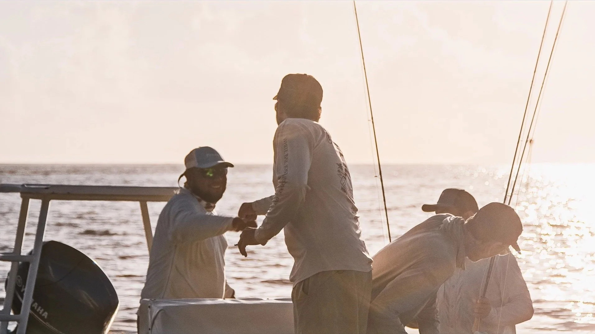 Four men on a boat at sunset, with two of them shaking hands and the others engaged in fishing activities.