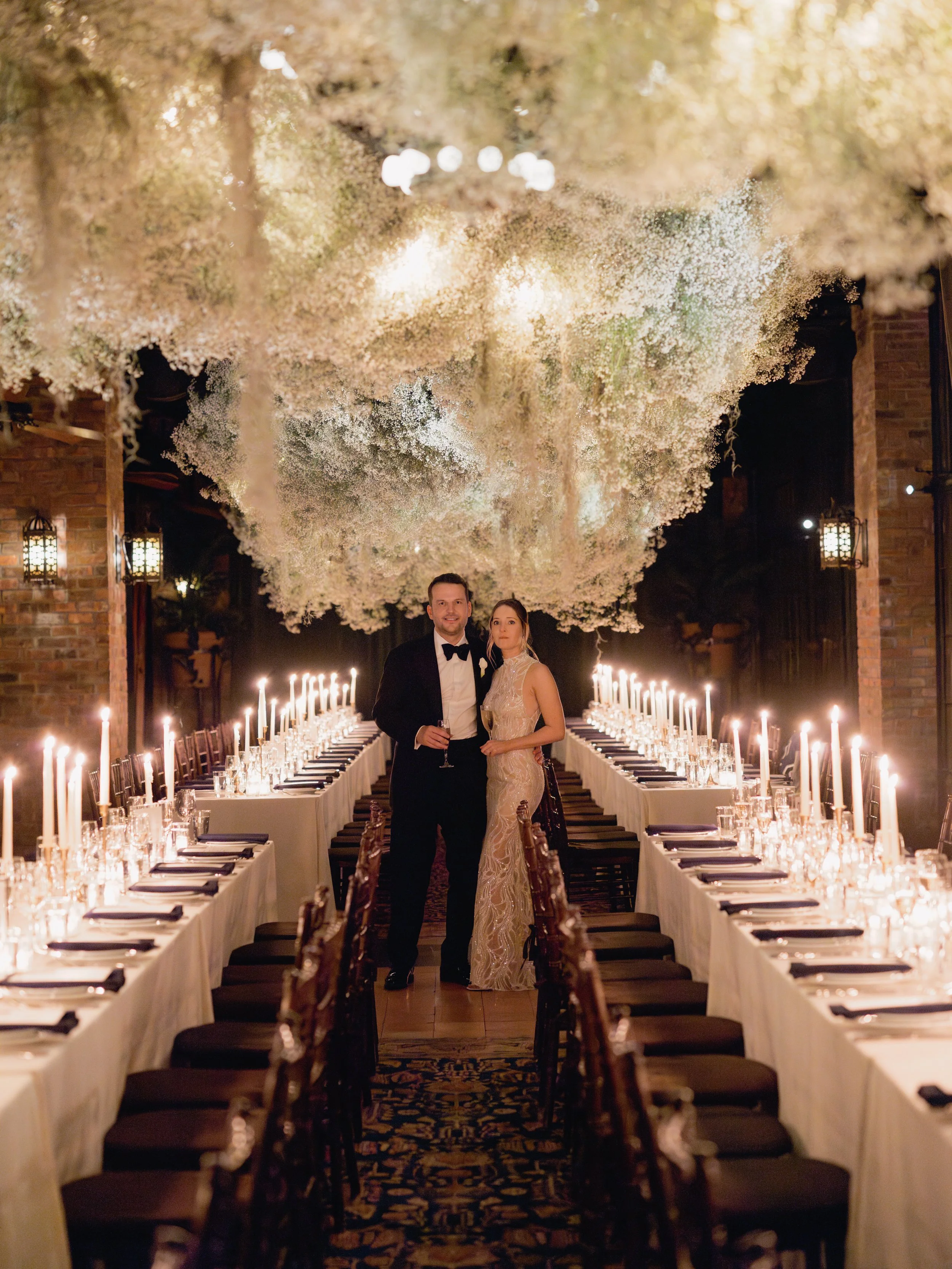 A couple dressed in formal attire standing under an elegant, floral ceiling installation at a wedding reception.