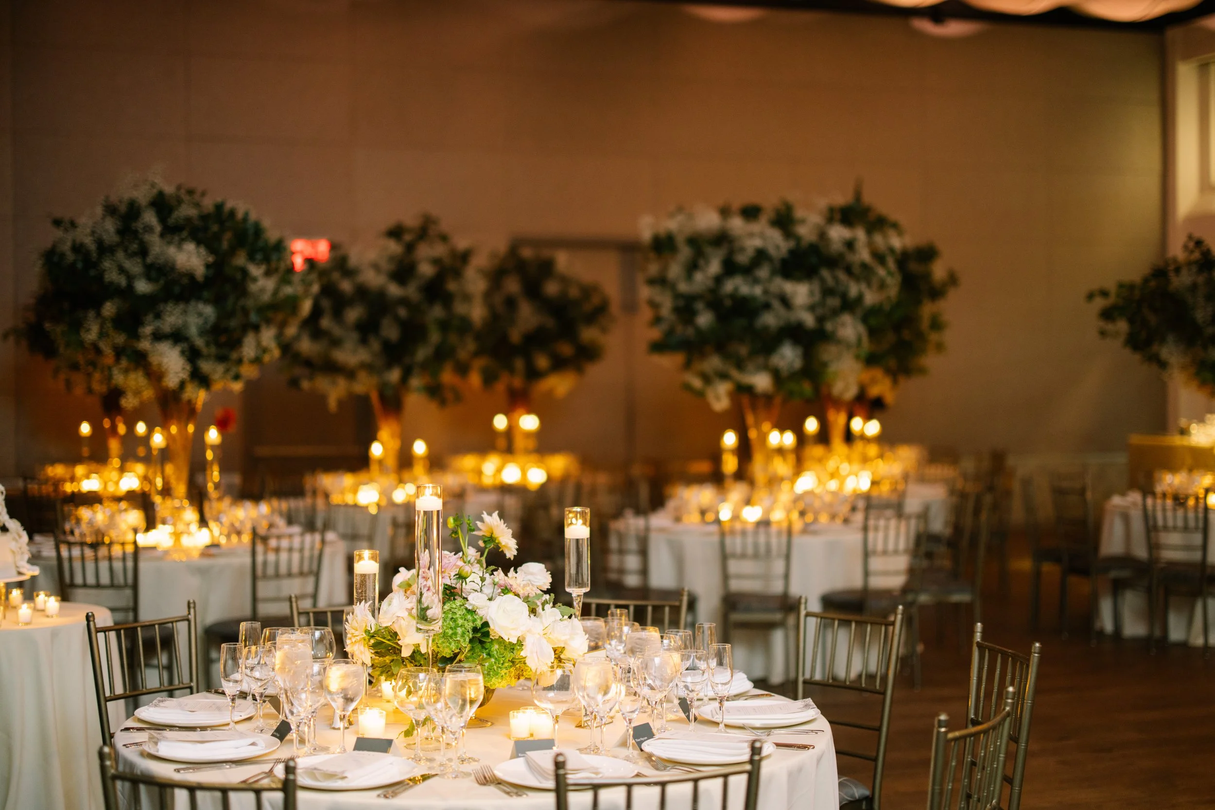 Elegant banquet hall decorated with lush floral arrangements, tall candle centerpieces, and warm ambient lighting for a formal event.
