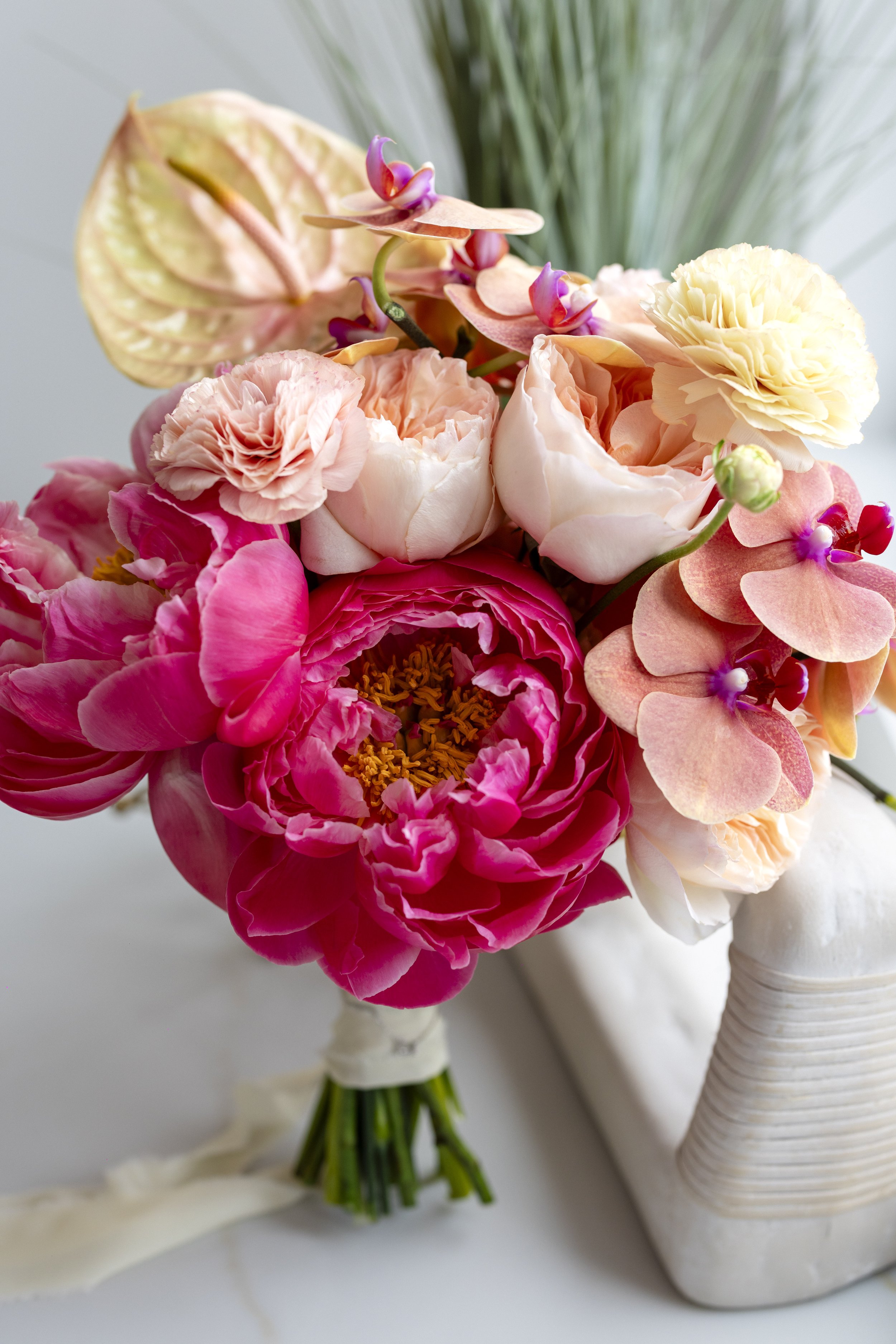 A bouquet of pink and cream roses, peonies, and orchids in a white vase.