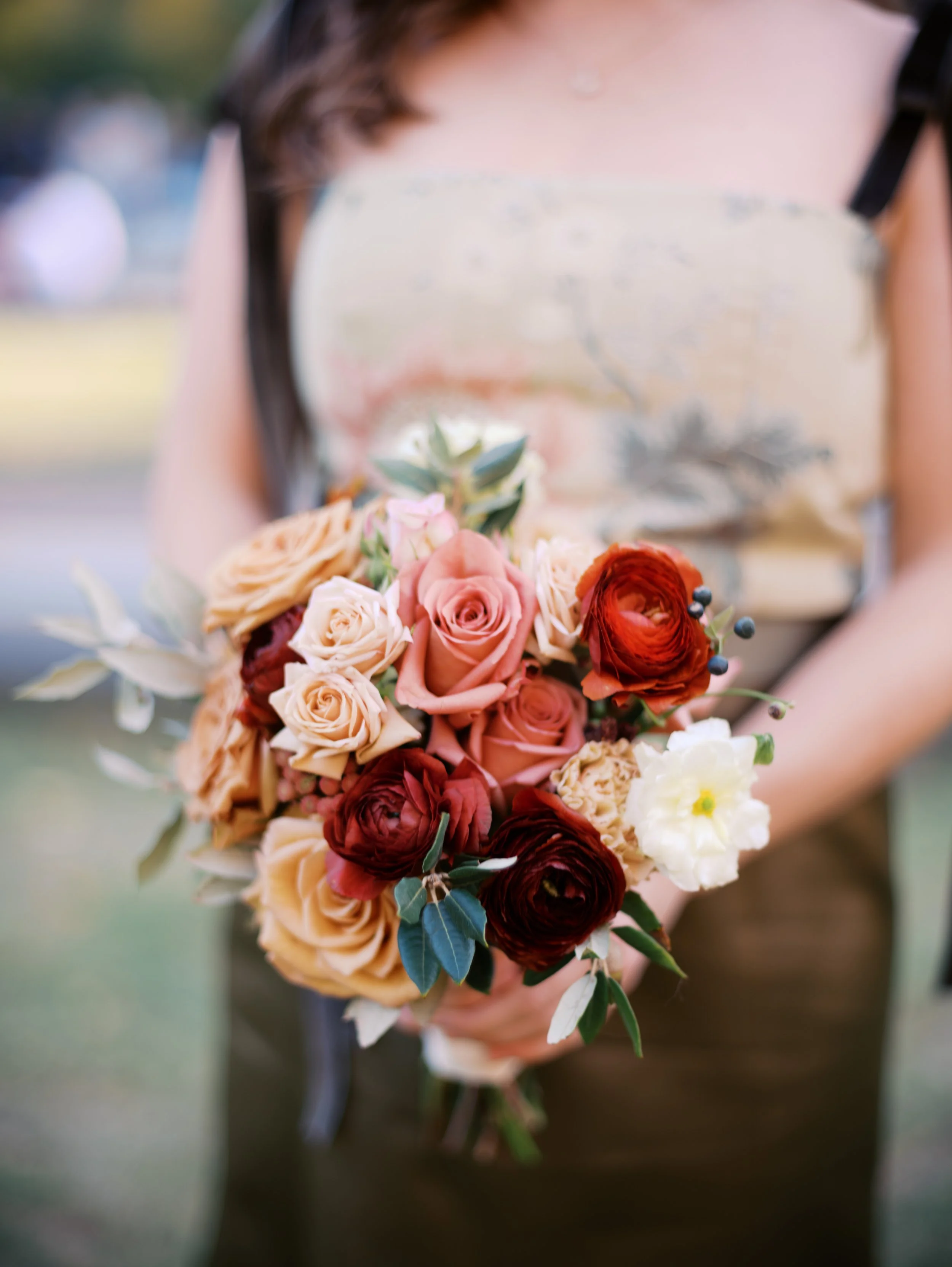 Person holding a bouquet of mixed roses and flowers, with a blurred outdoor background.