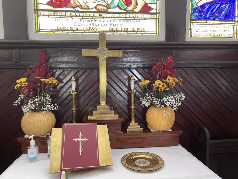 A church altar decorated with two vases of flowers, bees, and other flowers, a cross, and a candle holder with candles. A book with a crucifix on the cover is open in front of the altar.