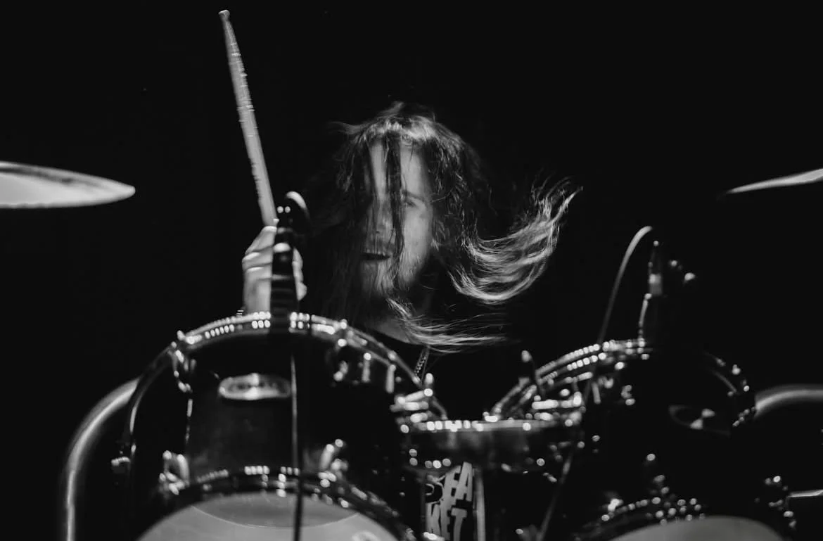 A man with long hair playing drums in a dark setting