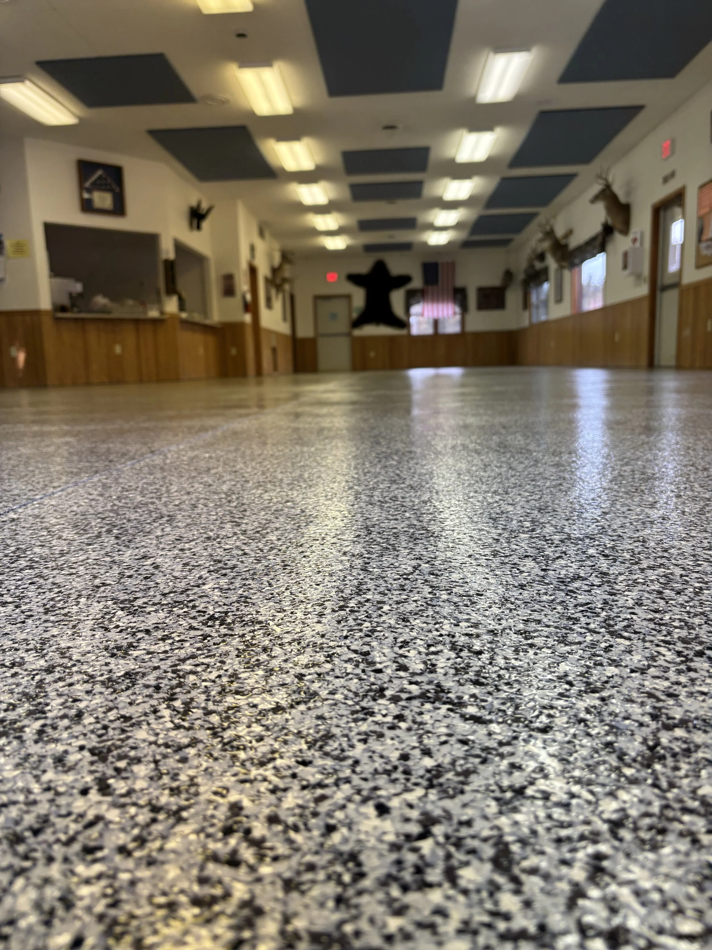 A room with a speckled tile floor, decorated walls with wood paneling, mounted animal heads, and a star-shaped decoration on the back wall. Fluorescent ceiling lights illuminate the space.