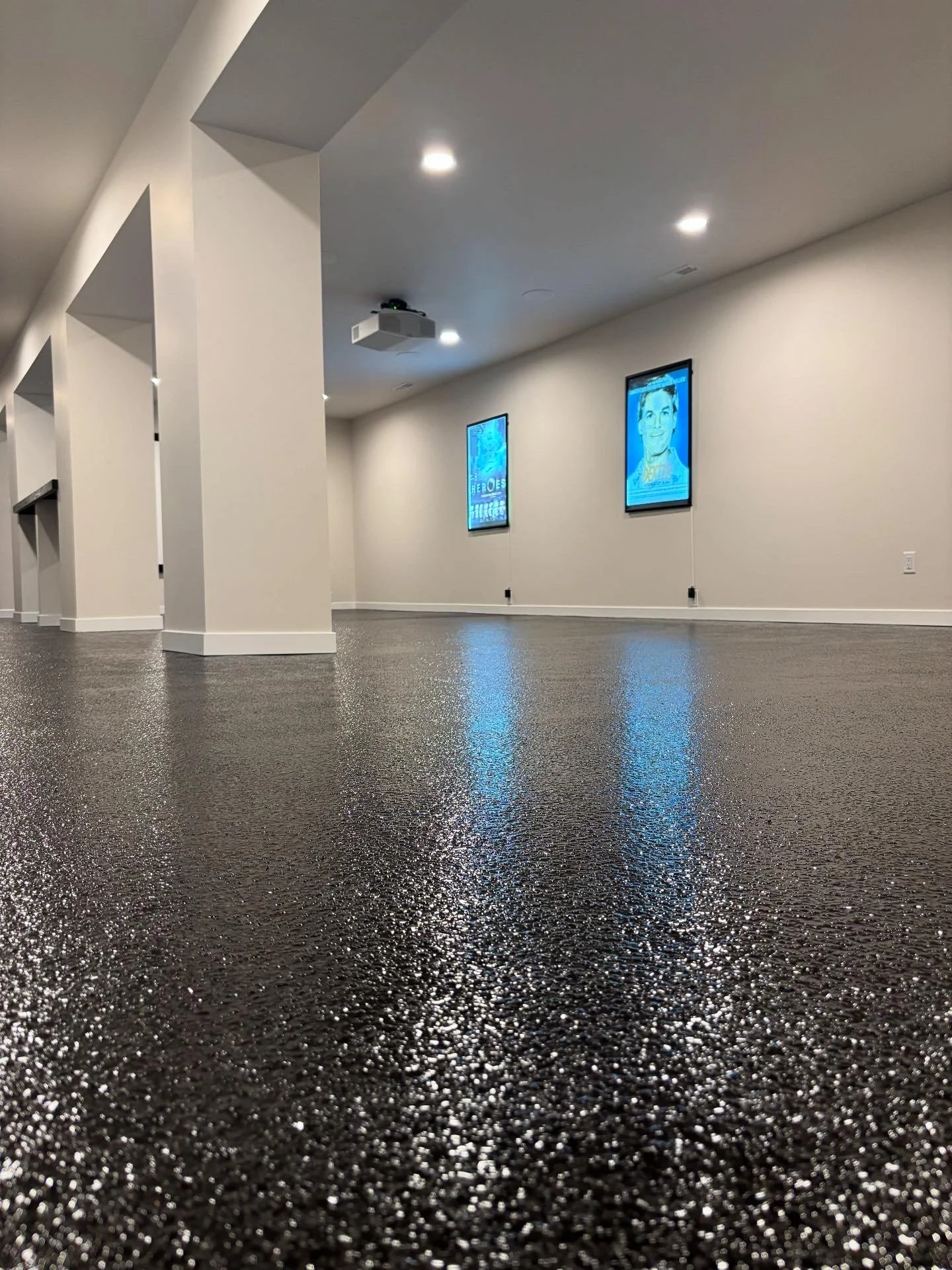 Empty indoor room with dark speckled flooring, white walls, digital screens on the wall, and ceiling lights.